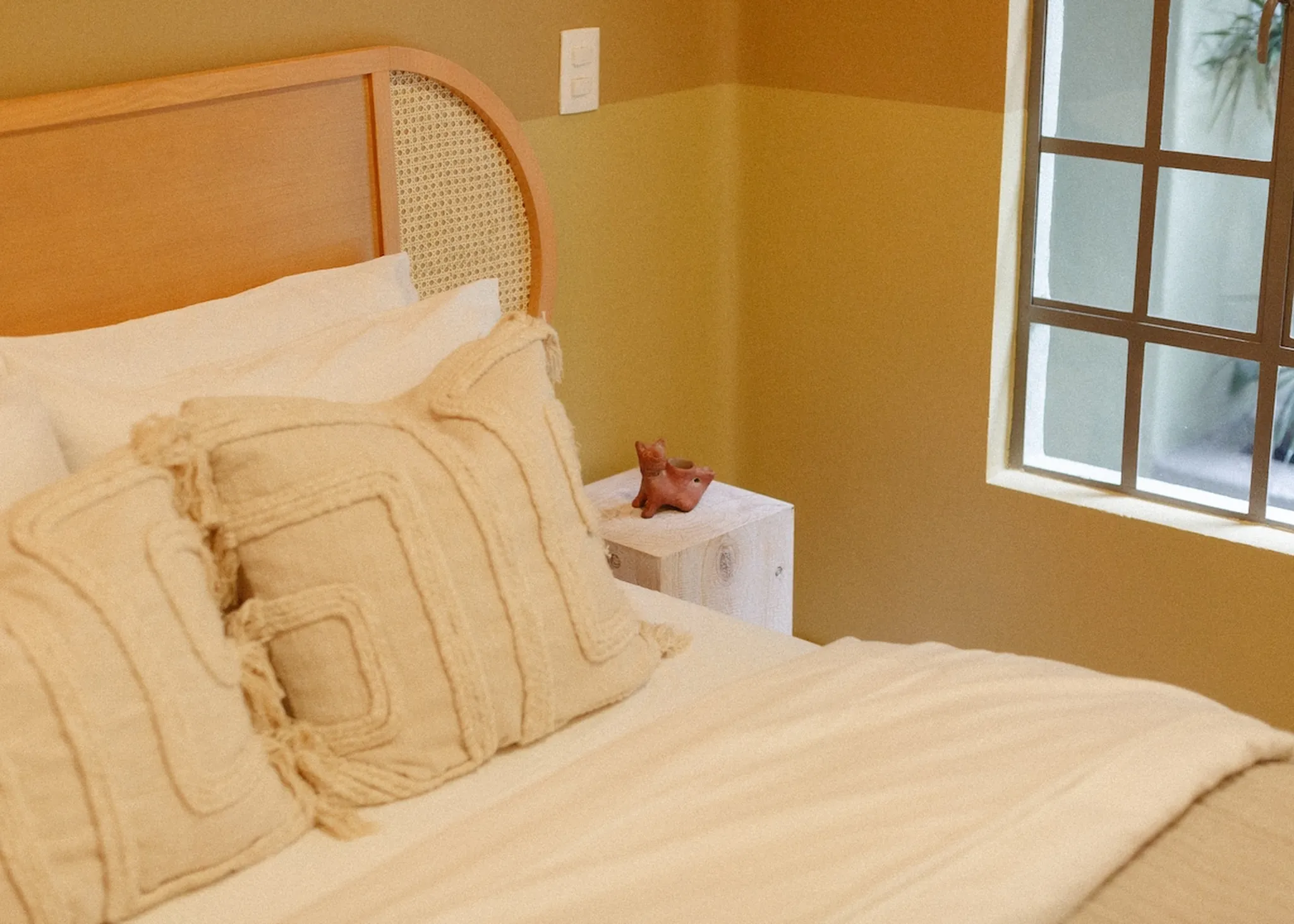 A close-up of a bed with textured cream pillows, a wooden headboard, and a window.