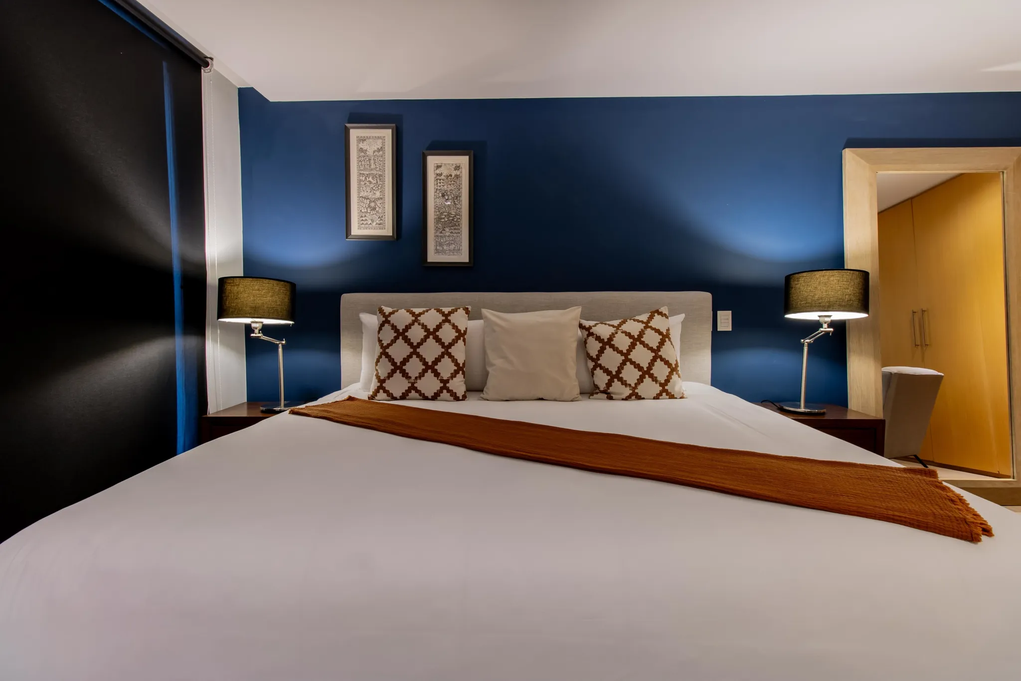 A bedroom with a large bed featuring white sheets, decorative pillows, and an orange throw.