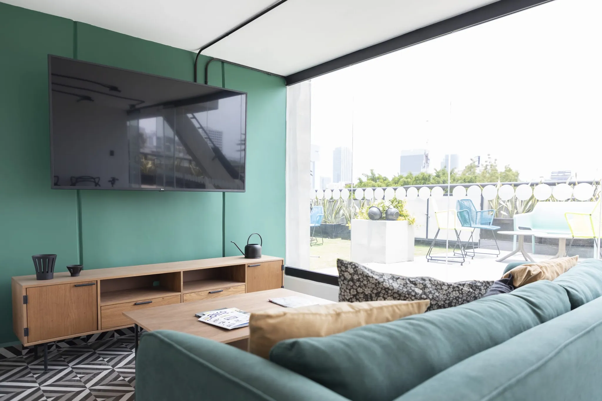 Modern living room with teal sofa, wooden media console, and large window with city view.