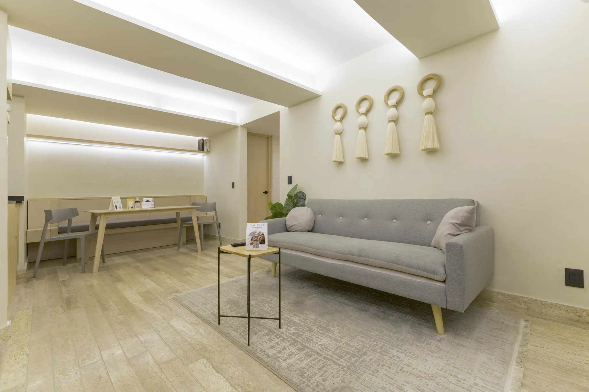 A living room with a gray sofa, a wooden table, chairs, and wall decor.