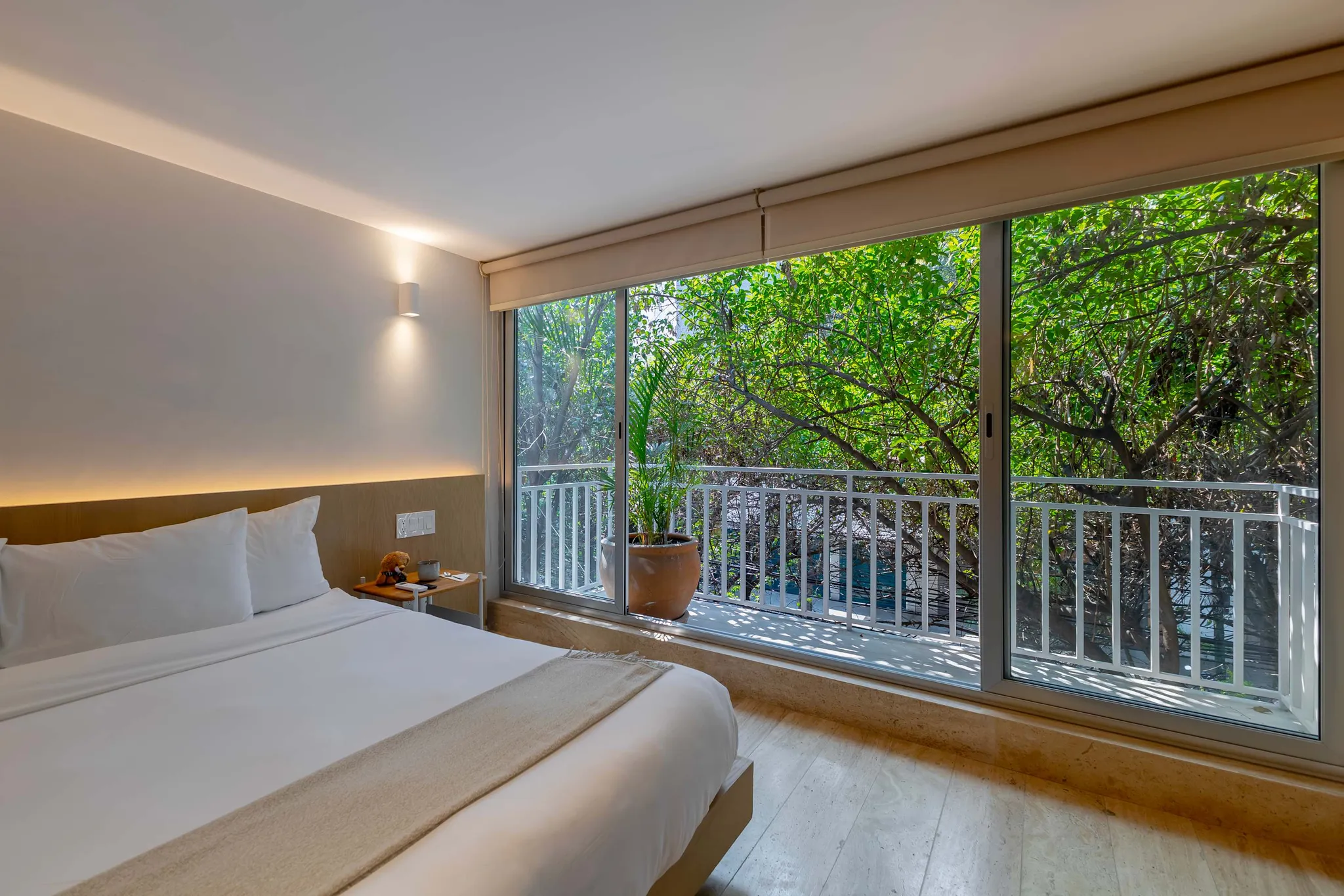 A modern hotel room with a bed, a nightstand, and a large window overlooking lush greenery.