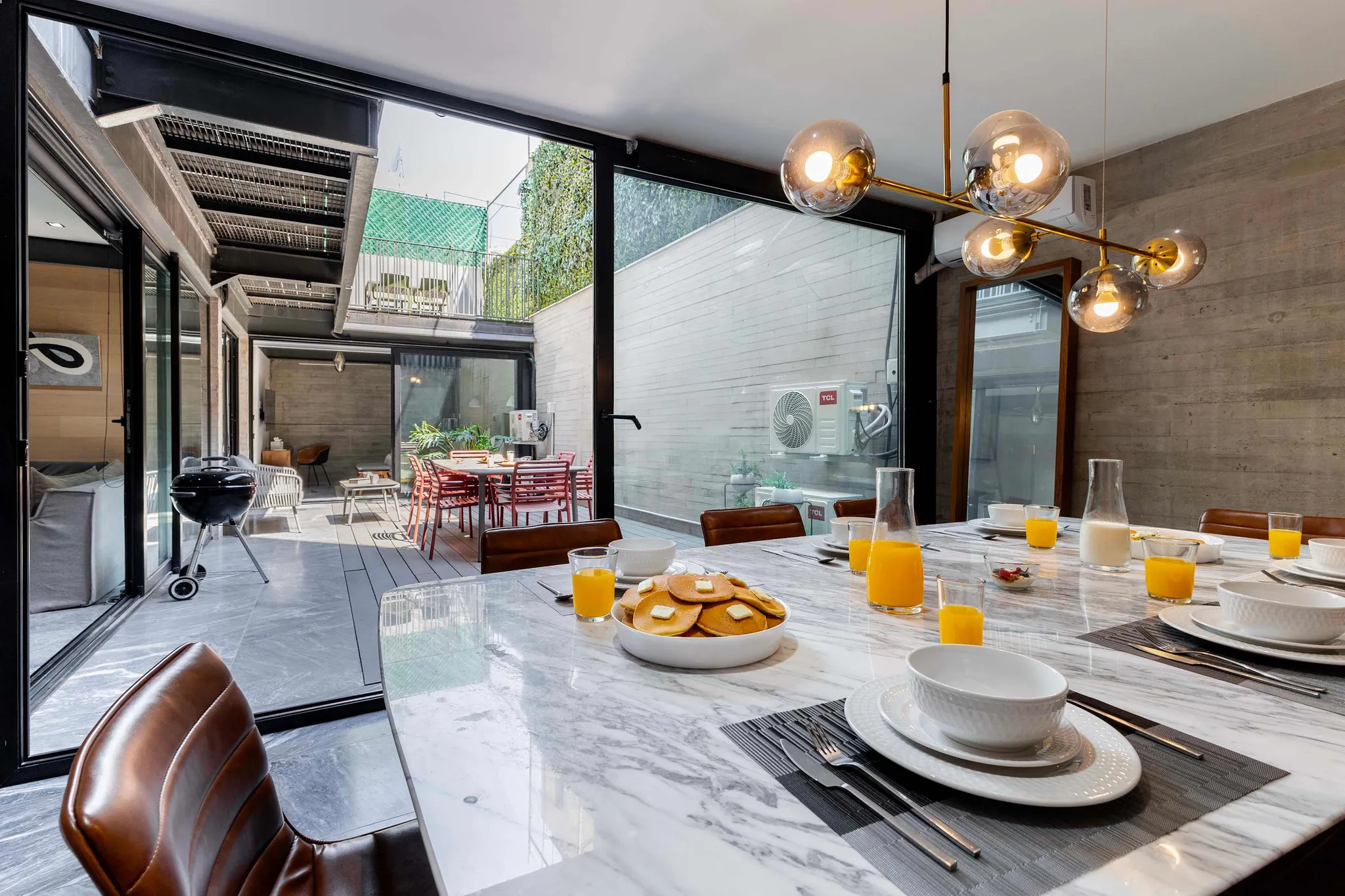 A modern dining area with a marble table set for breakfast and glass sliding doors opening to an out