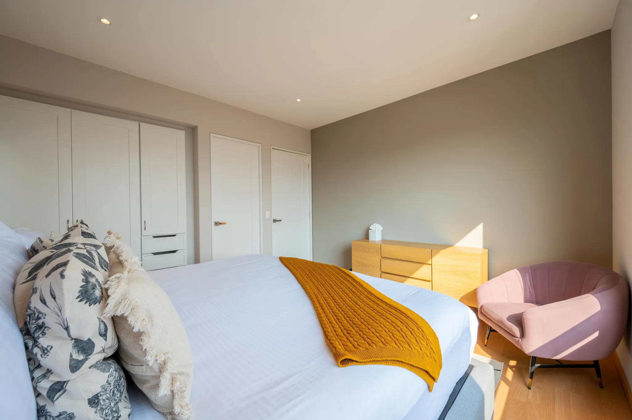 A bedroom with a bed, dresser, chair, and closets.