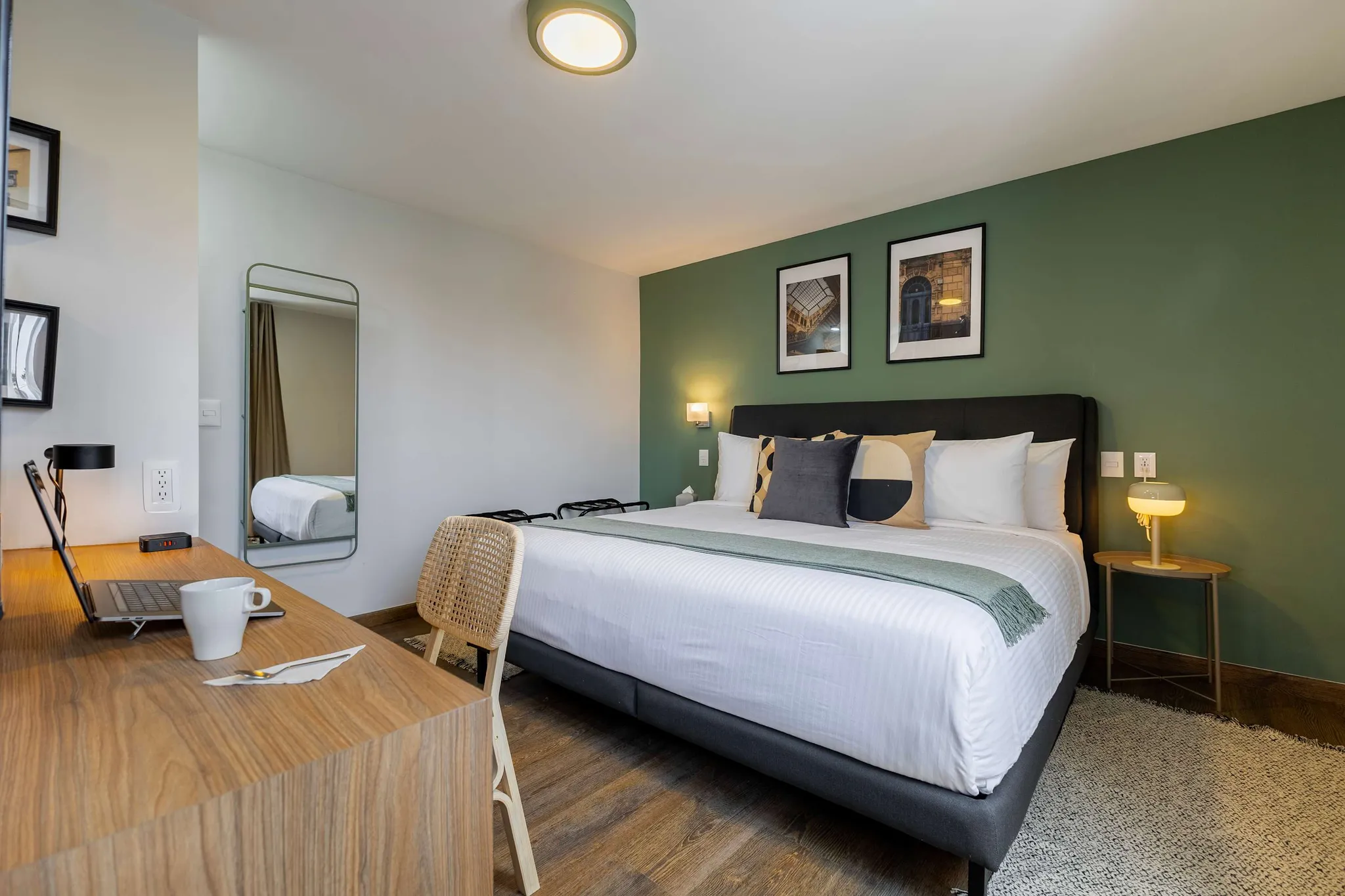 A modern bedroom with a large bed, a desk, and a mirror.