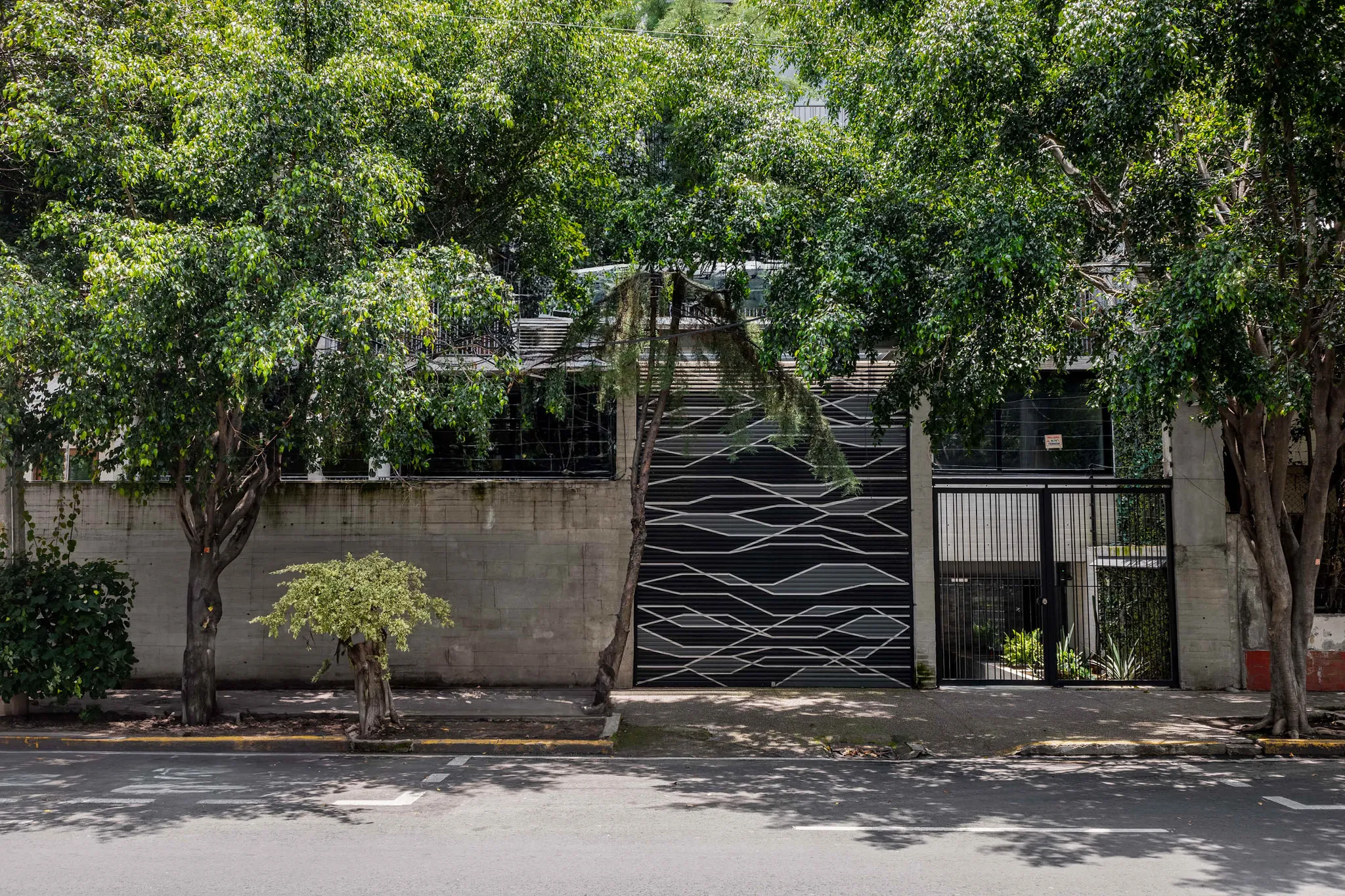Modern building with abstract facade and gate, flanked by trees.