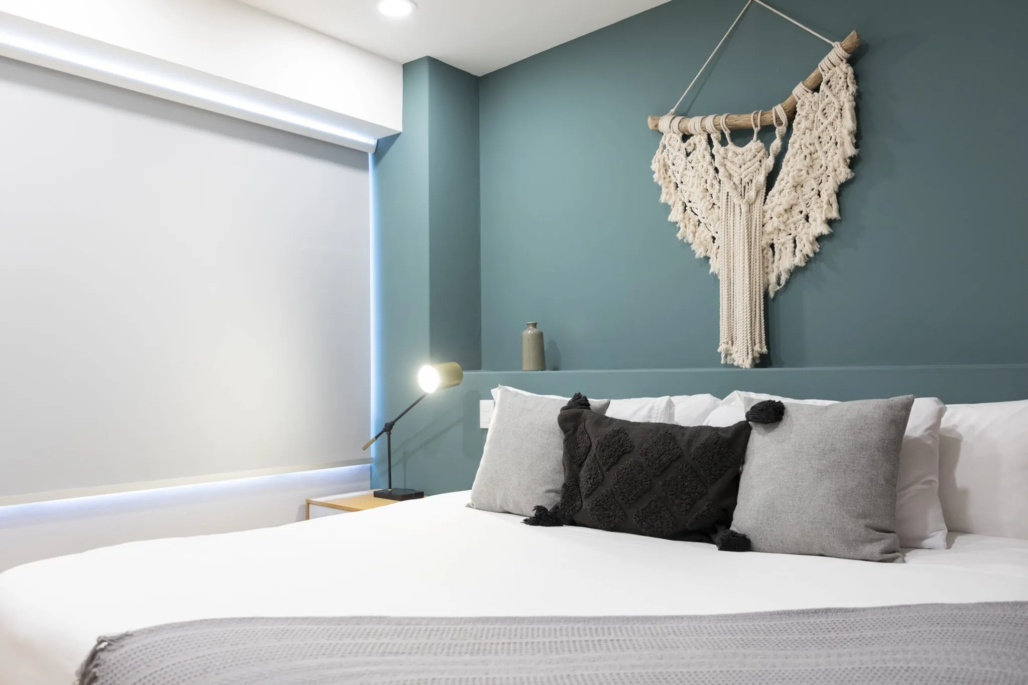 A modern bedroom with a white bed and teal wall featuring macrame wall decor.