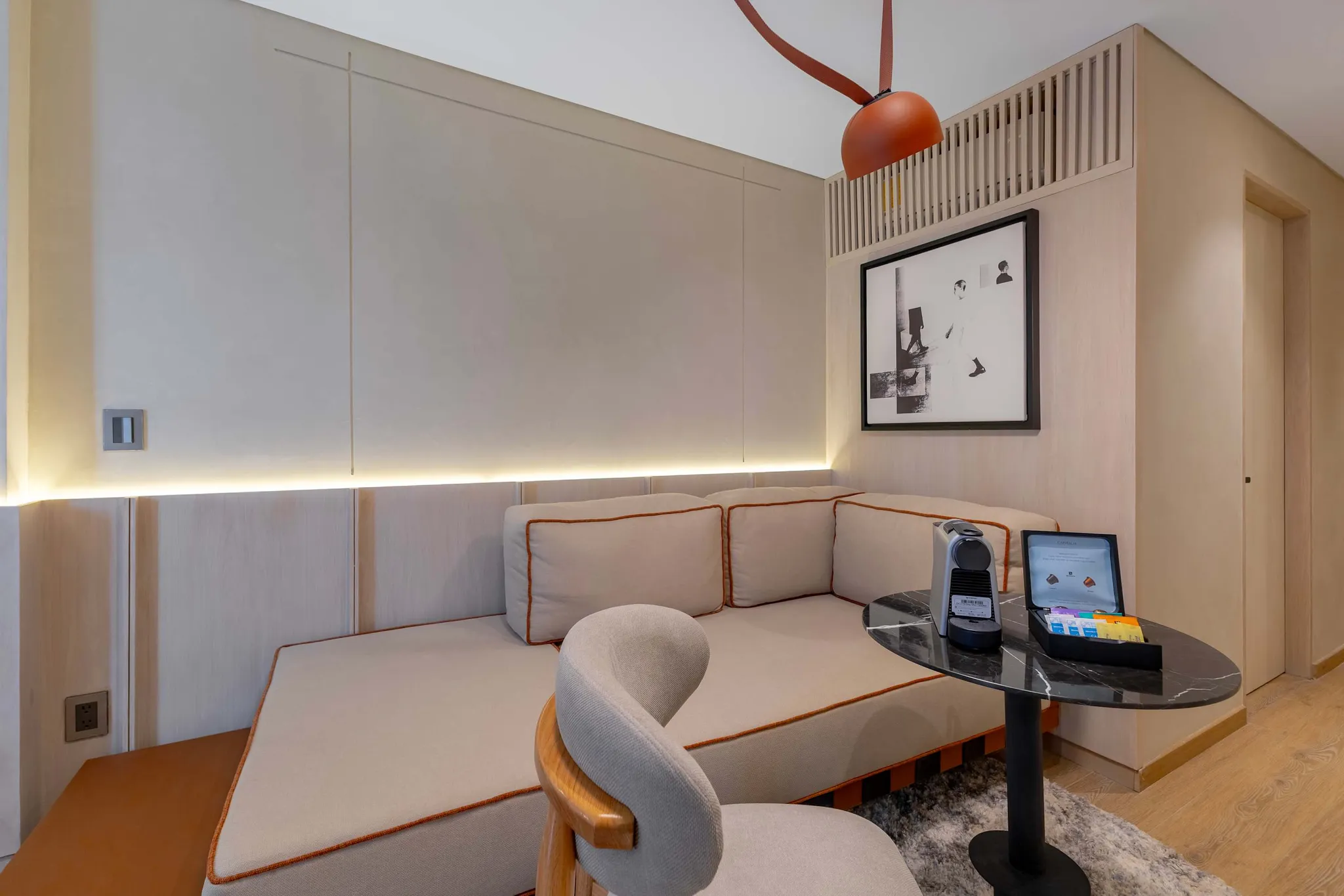 A modern hotel room with a couch, chair, table, and coffee maker.
