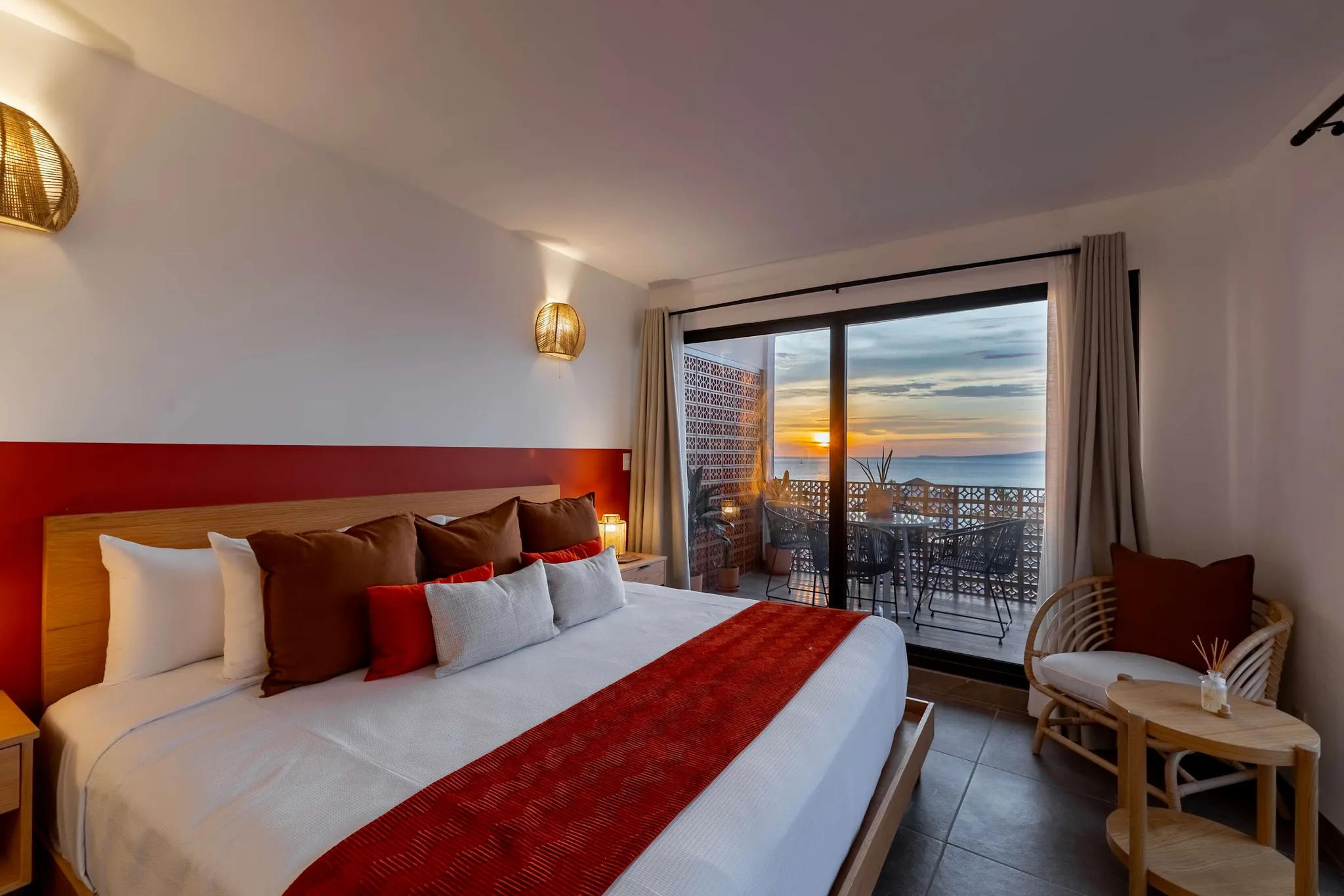 A luxurious bedroom with a king-size bed facing a balcony with a sunset view.