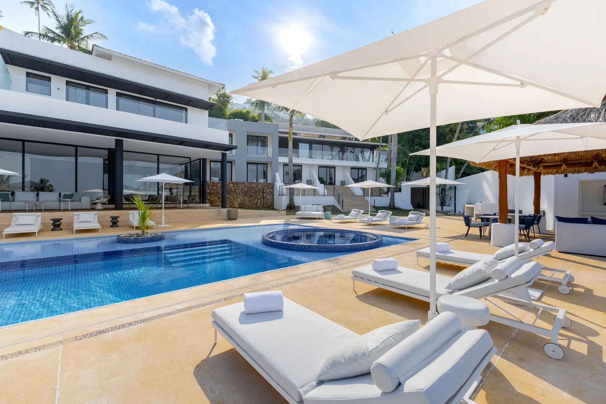 A modern villa with a pool and lounge chairs sits nestled in a tropical hillside.