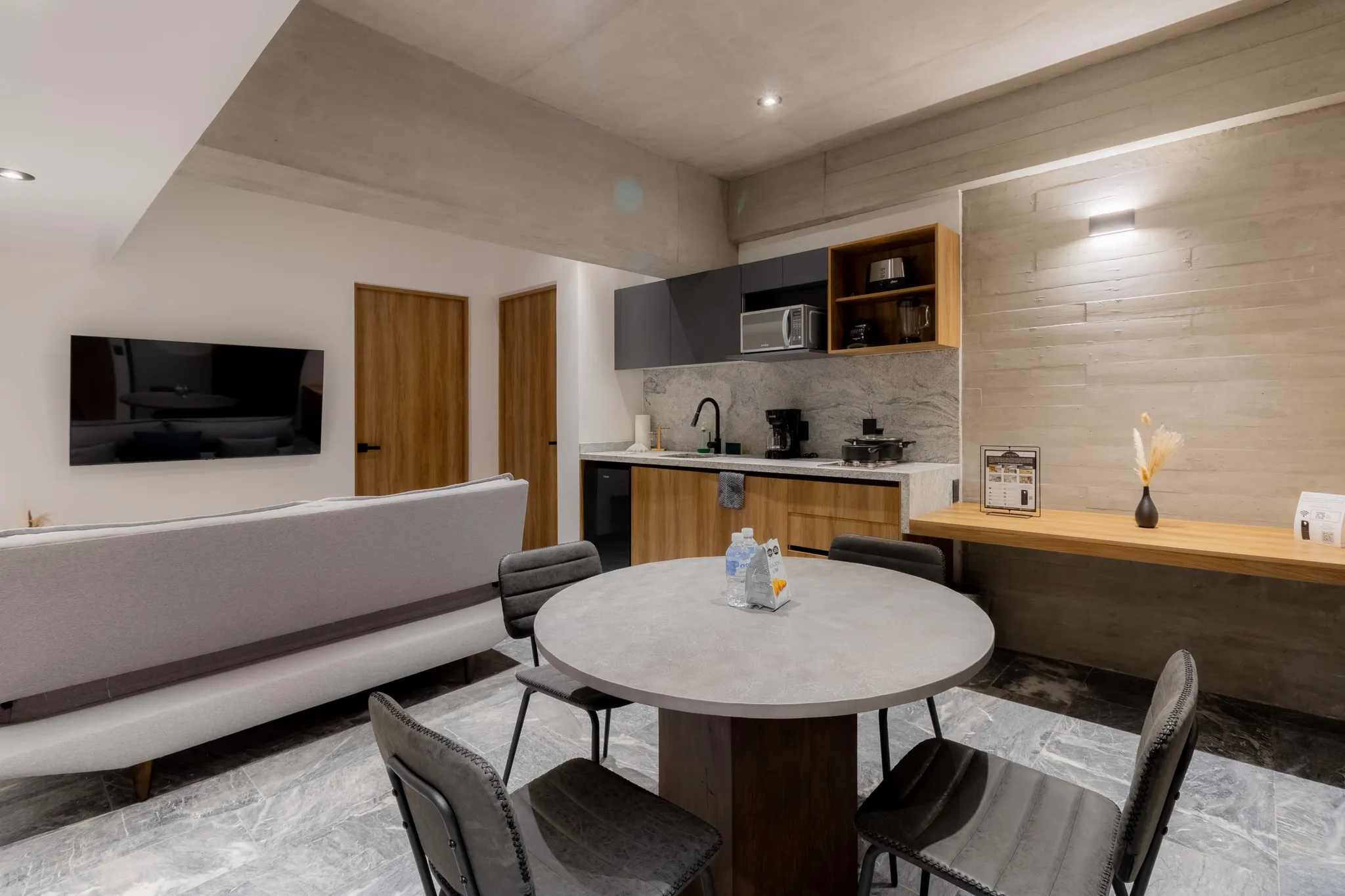 A modern dining area with a grey circular table and chairs in front of a kitchen.