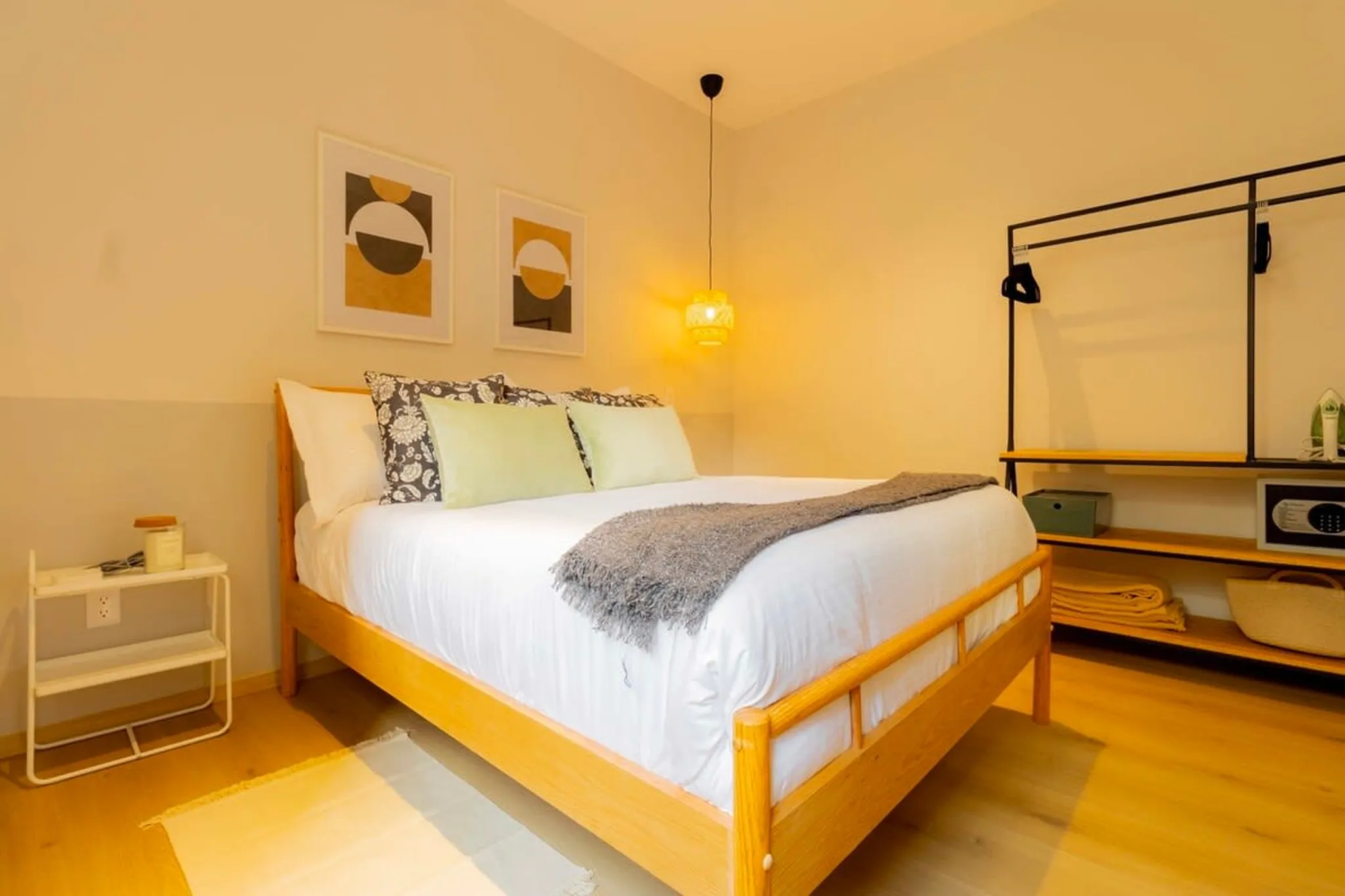 A cozy bedroom with a wooden bed, two abstract art prints, and a clothing rack.