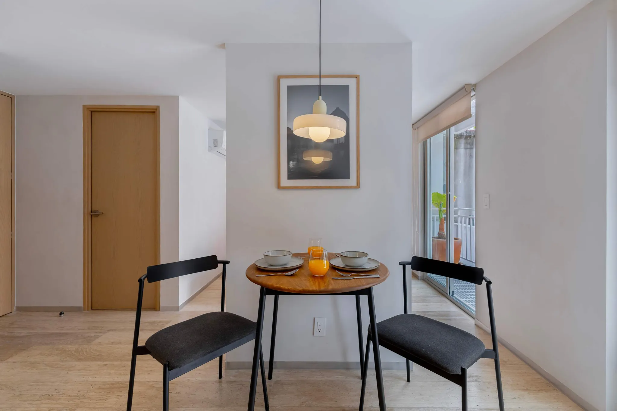 A dining table for two with orange juice and bowls sits in front of a balcony.