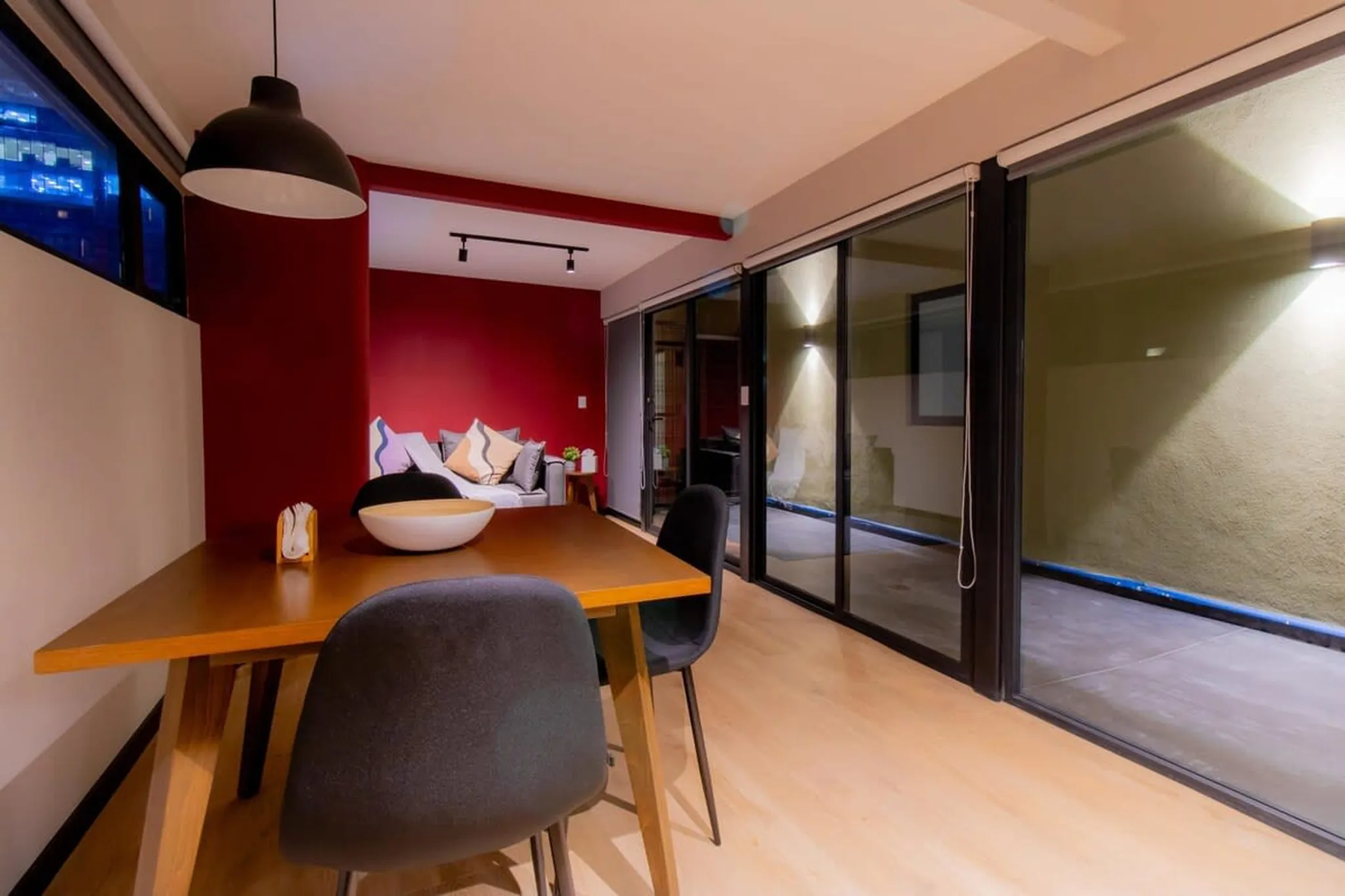 A dining room with a modern design, featuring a wooden table and chairs, with a red accent wall.