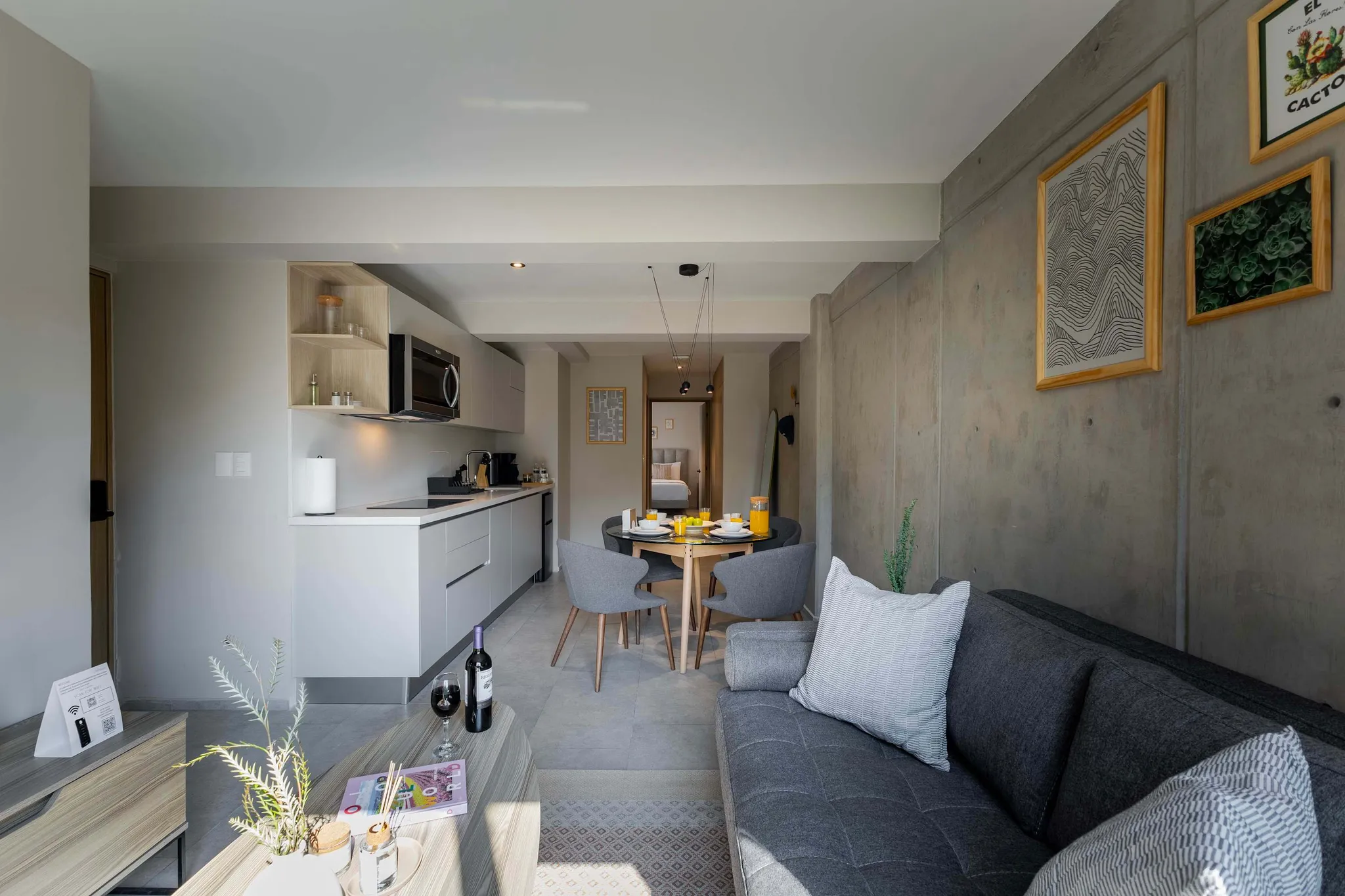 Modern living space with kitchen, dining area, and living room featuring gray furniture and artwork.