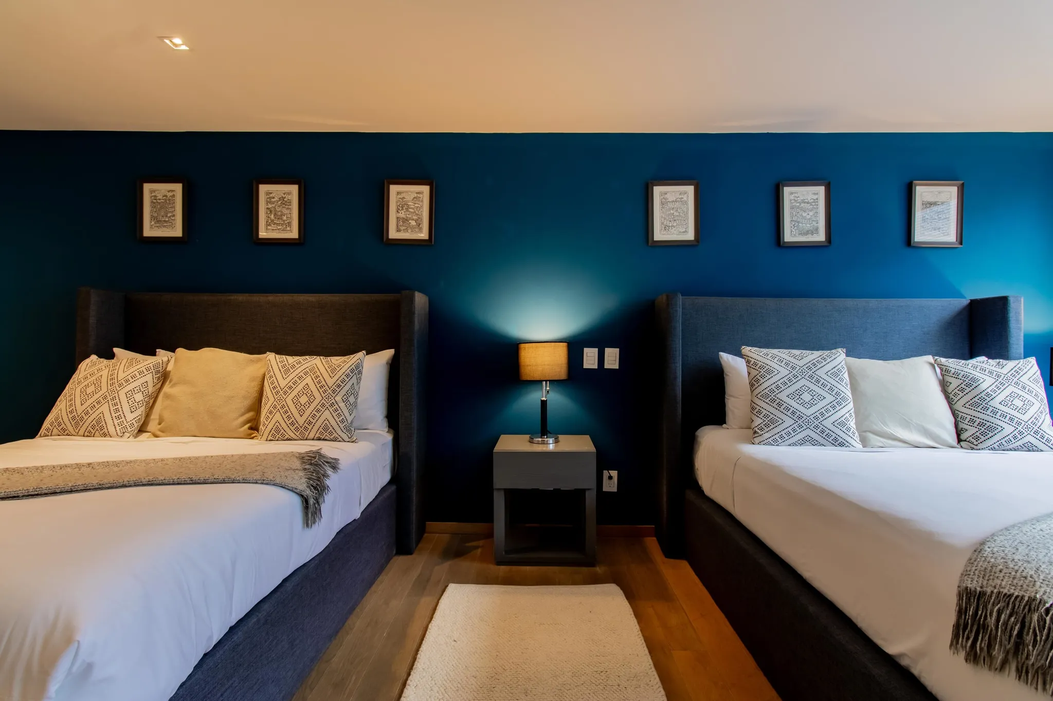 A bedroom with two beds, a blue wall, and framed art.