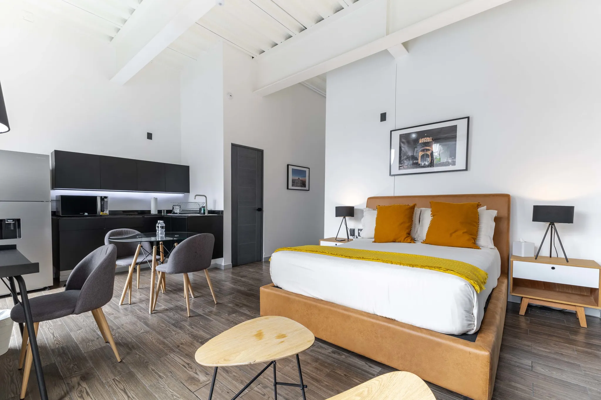 A modern studio apartment with a king-size bed, kitchen area, and dining table.
