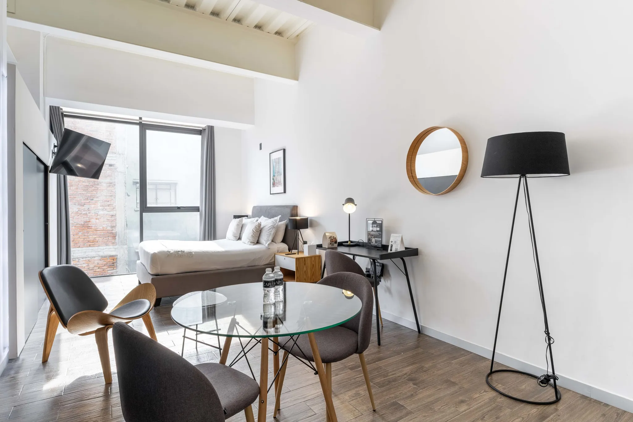 A studio apartment with a bed, desk, chairs, and a round glass table.