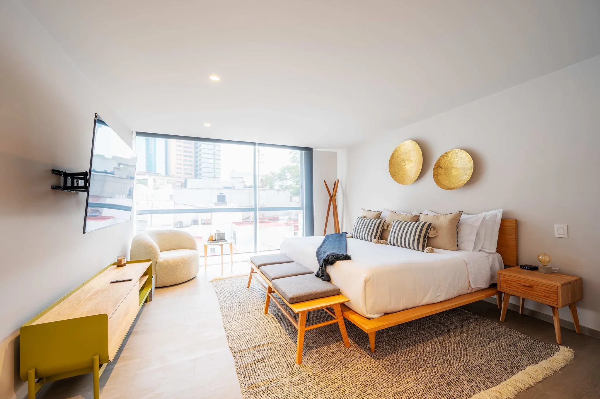 A modern bedroom with a king-size bed, a large window, and a wall-mounted TV.