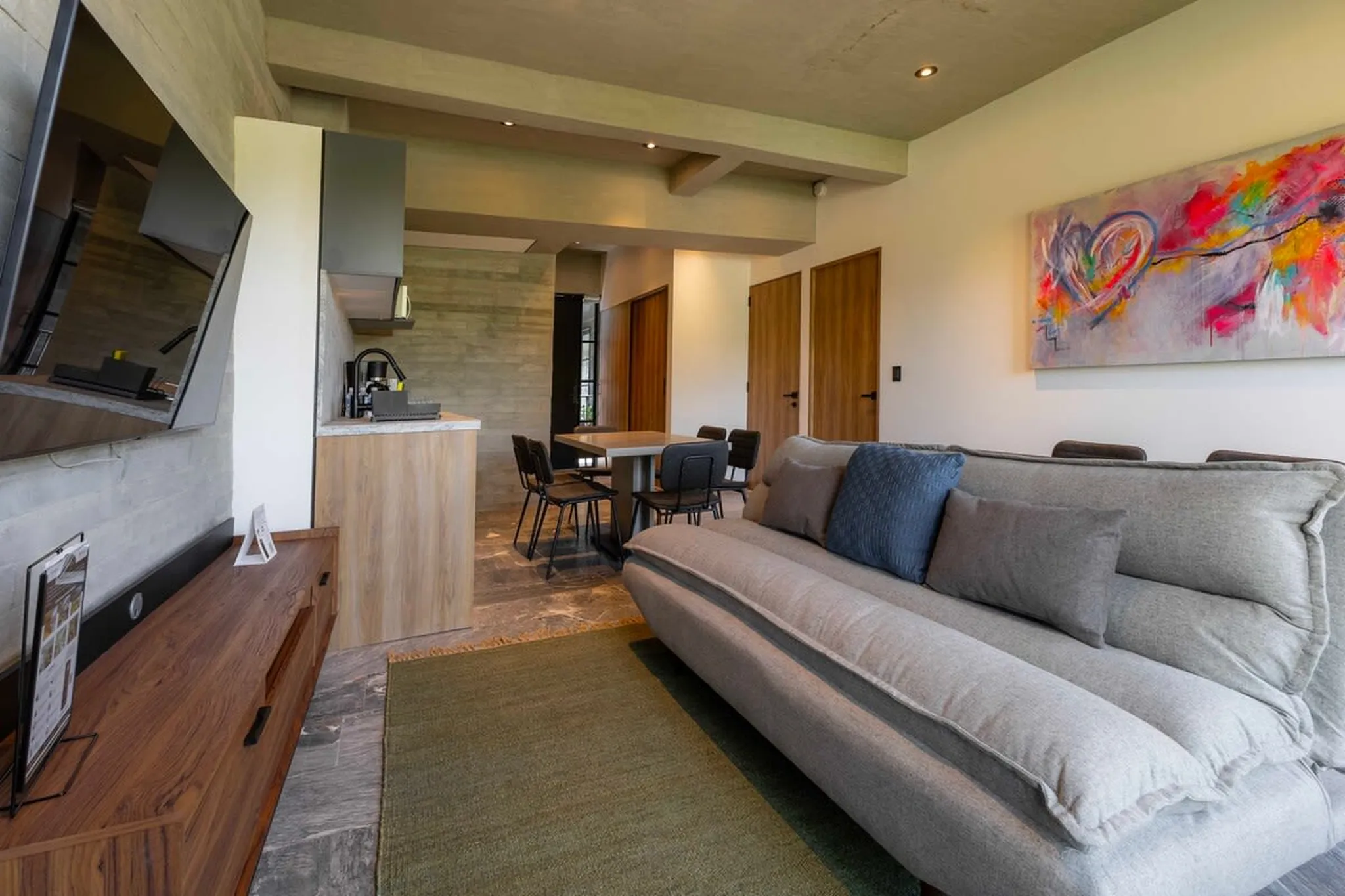 A modern living room with a gray couch, colorful abstract art, and a dining area.
