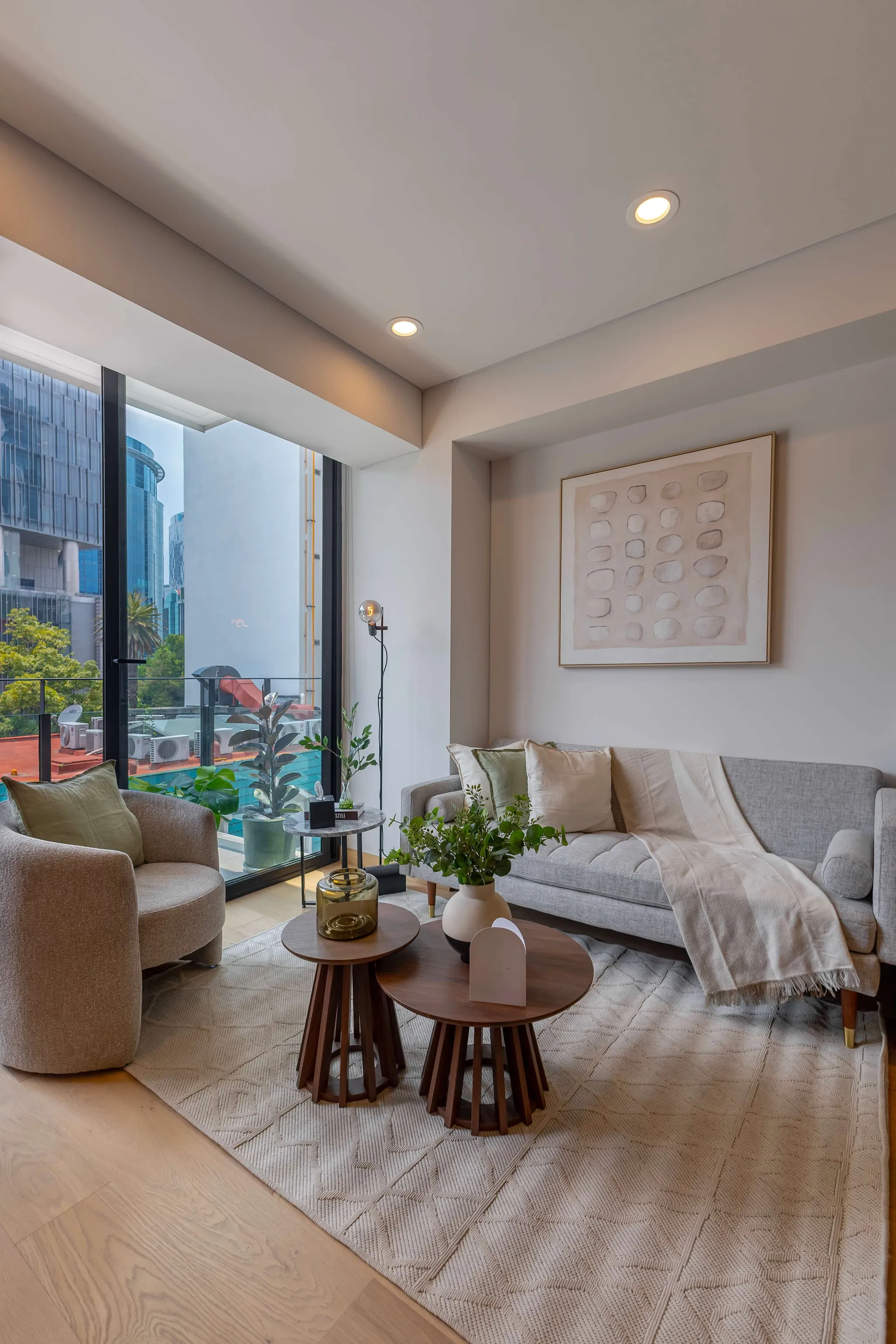 Living room with a gray sofa, armchair, coffee tables, rug, and large window with city view.