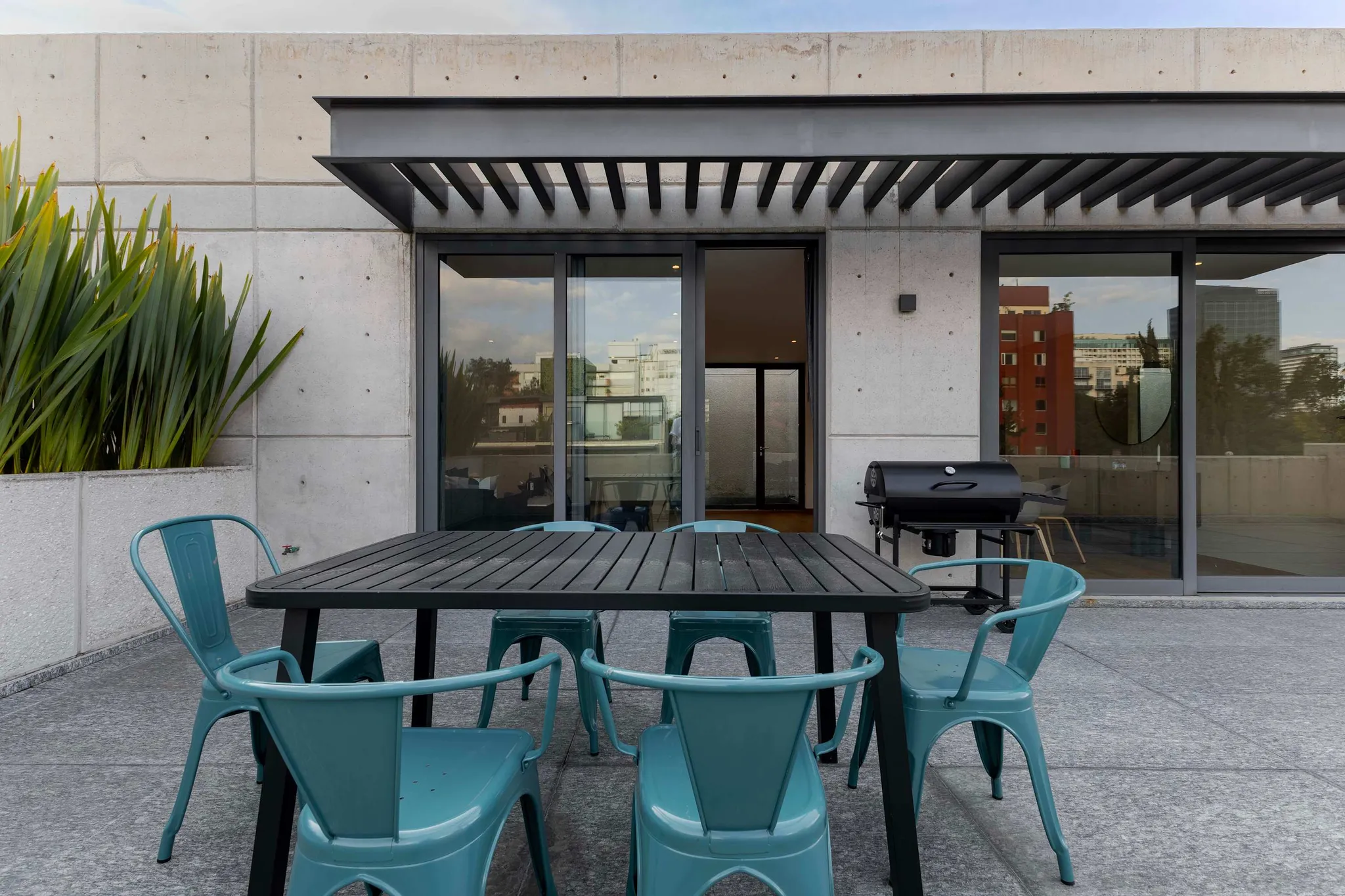 Outdoor patio with table, chairs, and grill, overlooking city buildings.