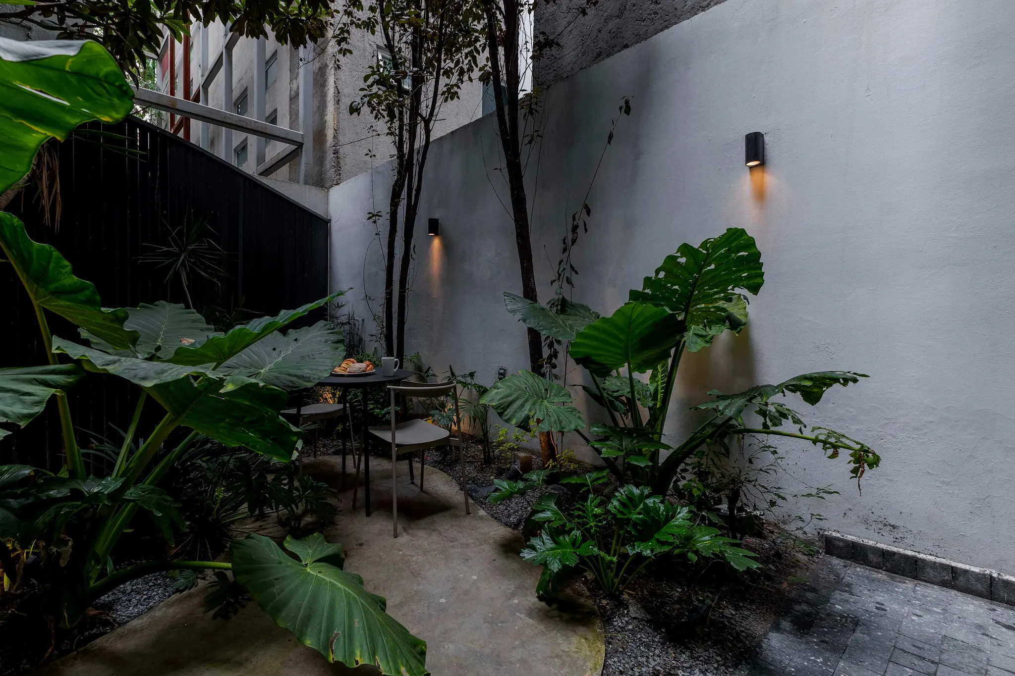 A serene patio with lush greenery and a small table set for breakfast.