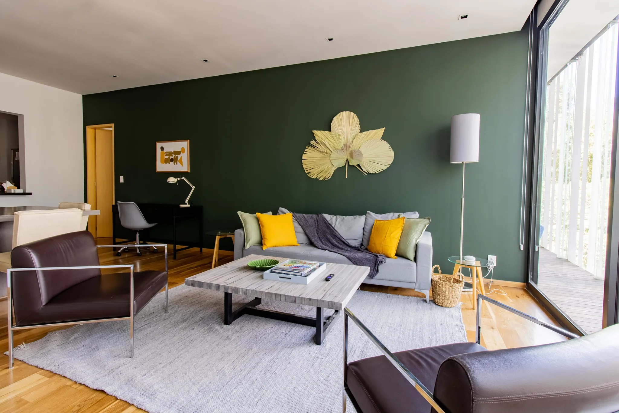 A modern living room with a green accent wall, a gray sofa, and brown leather armchairs.