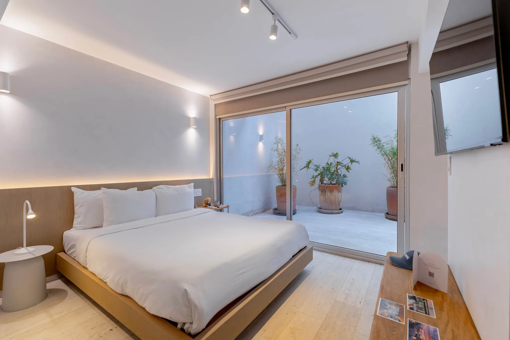 A modern hotel room with a bed, patio doors, and plants.