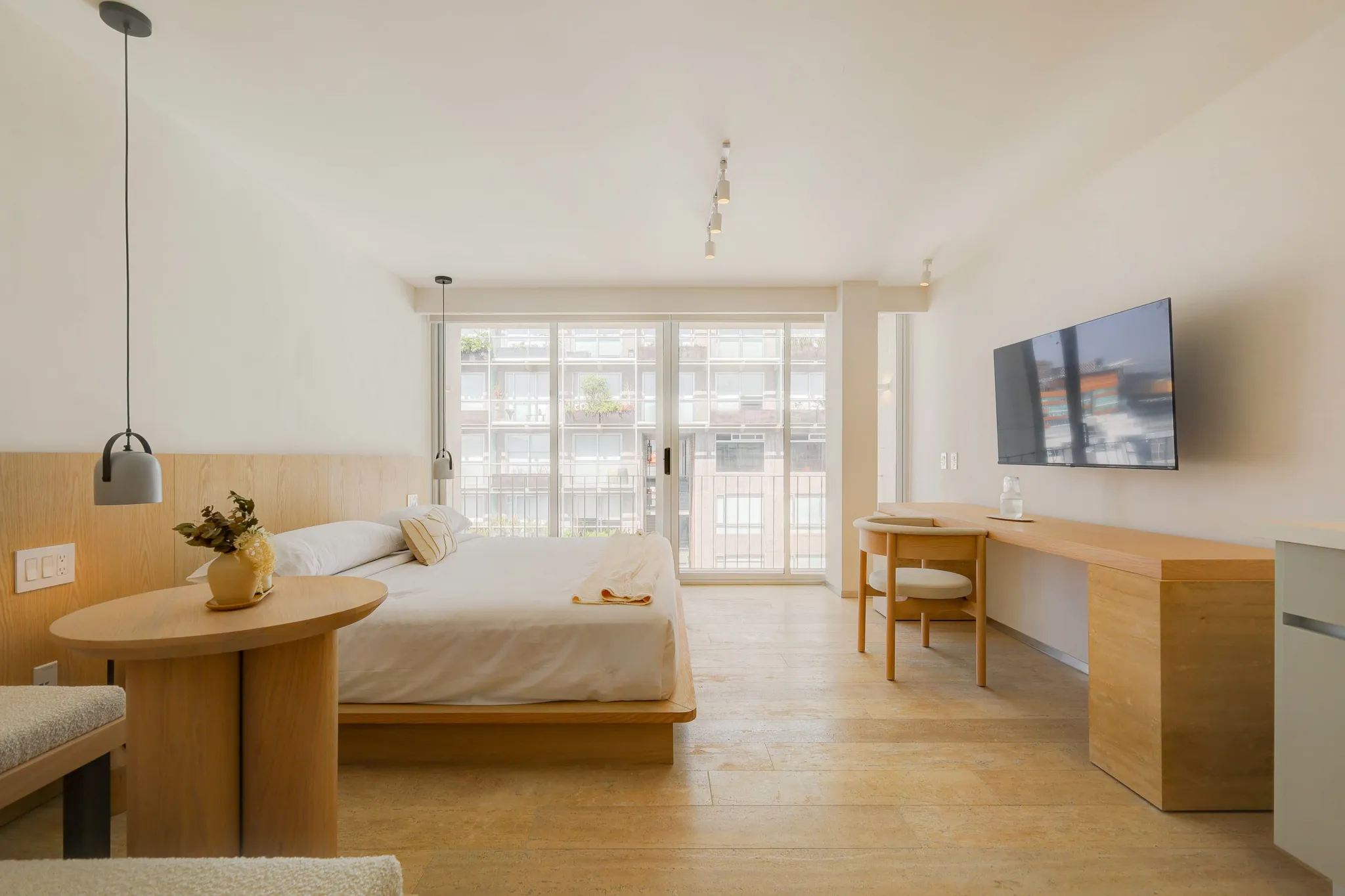 A bright, modern bedroom with a large bed and a wooden desk.