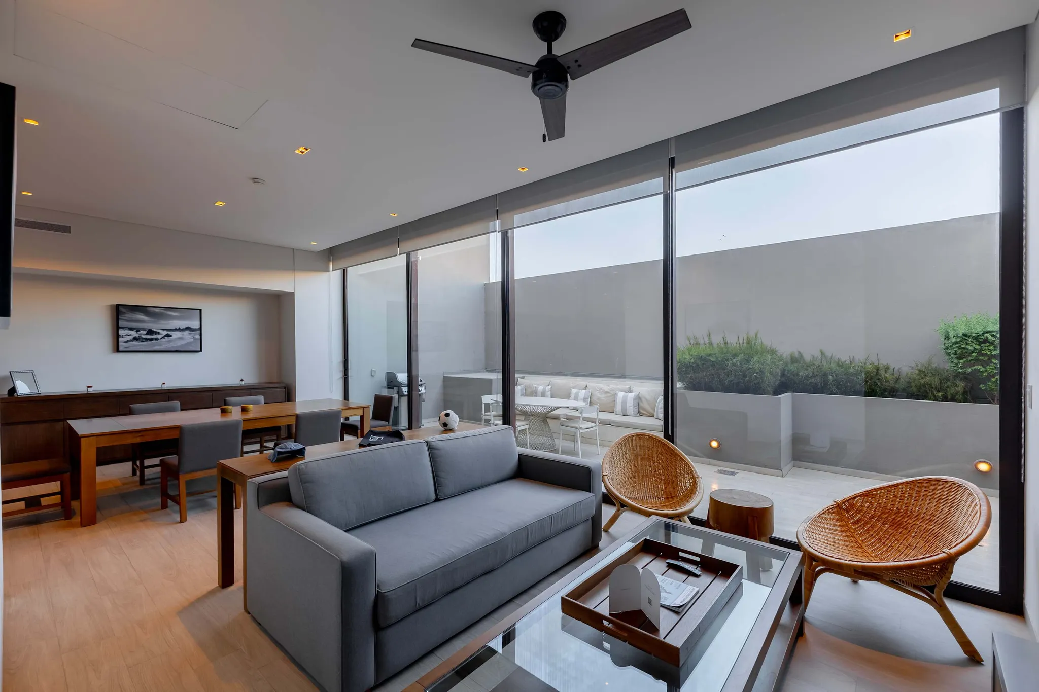 A modern living room with a gray sofa, wicker chairs, and a glass coffee table.