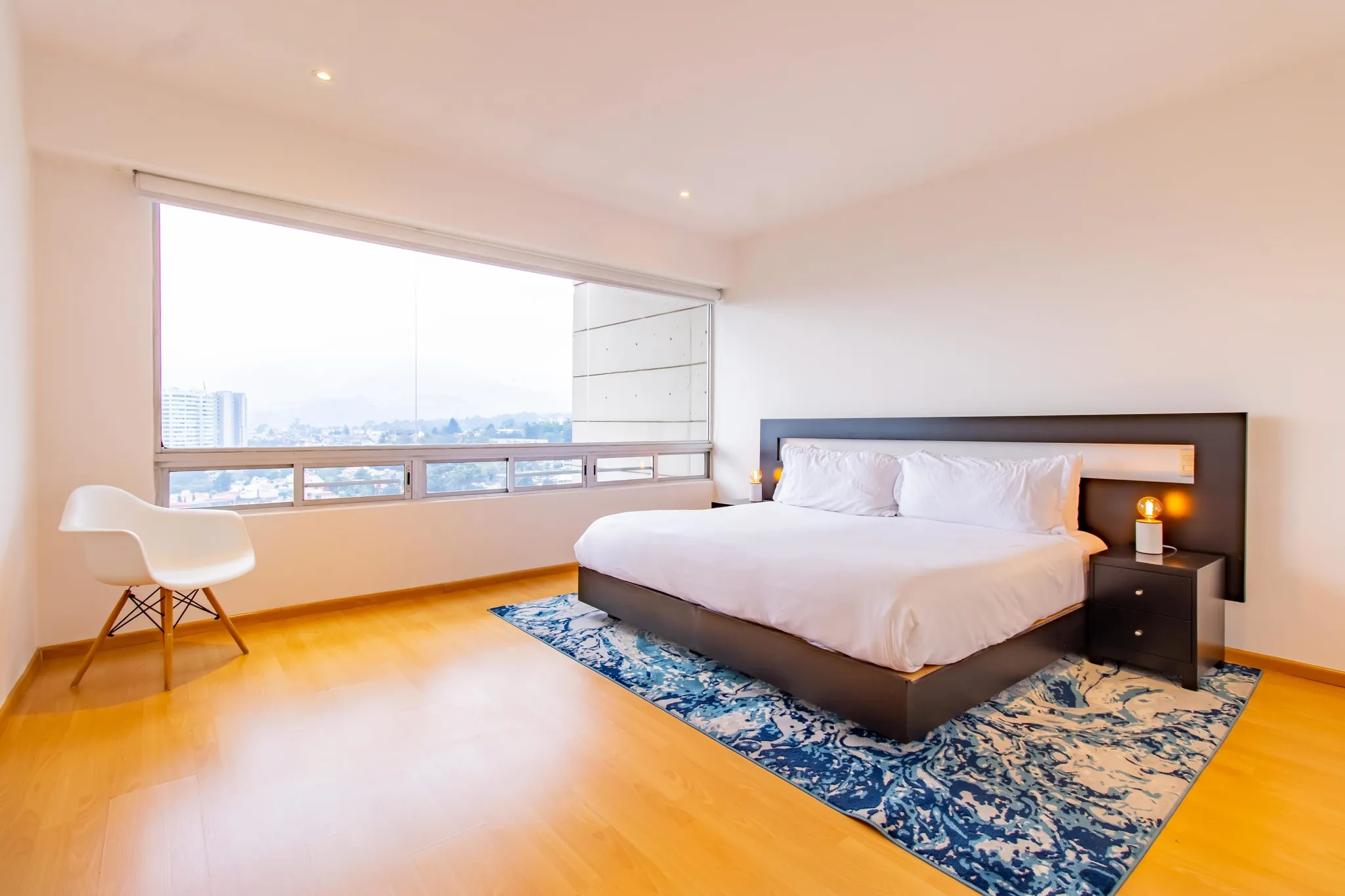 A white bed with pillows and nightstands sits on a blue rug in a bedroom.