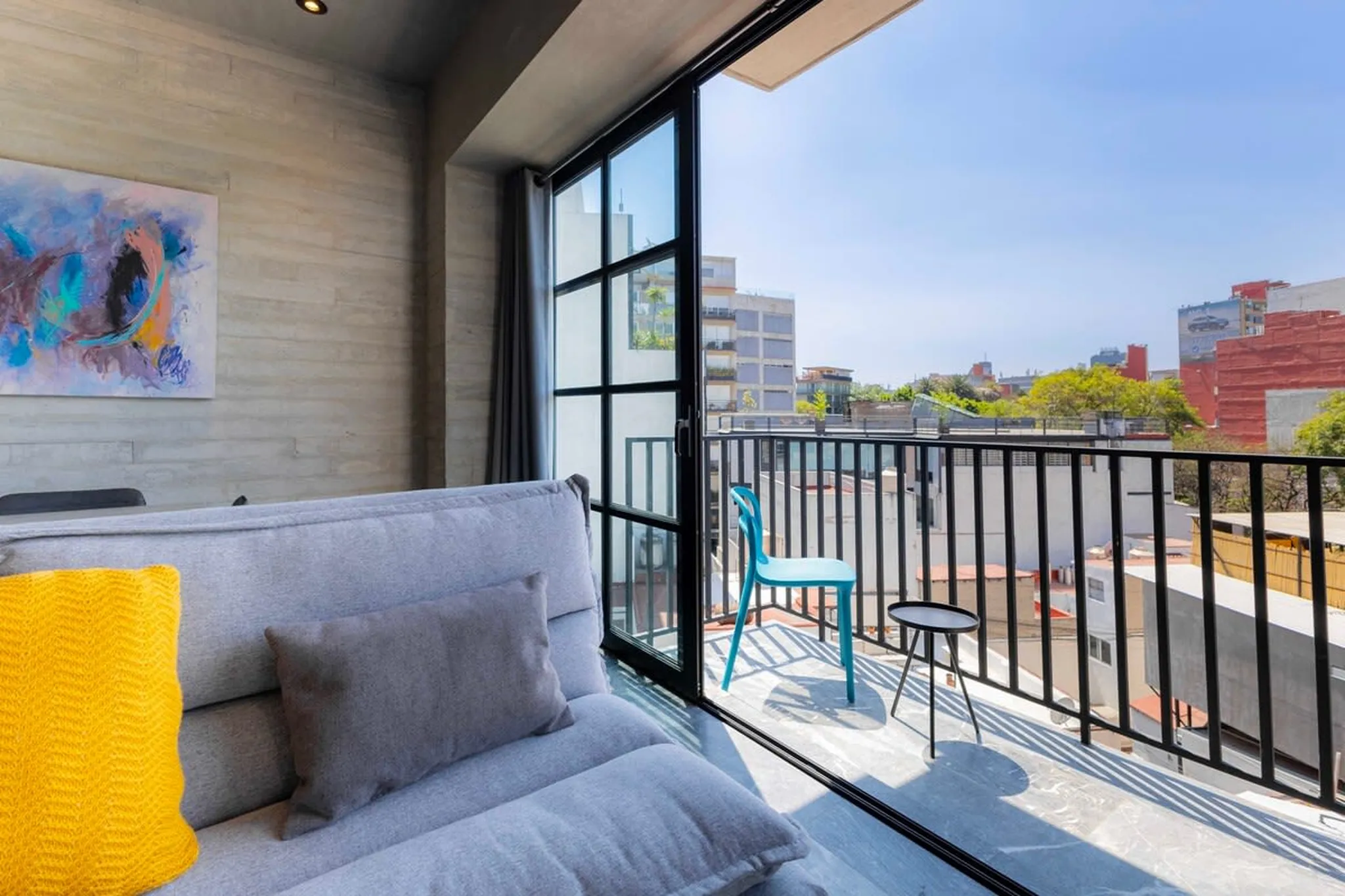 A living room with a grey couch and a balcony with a blue chair.