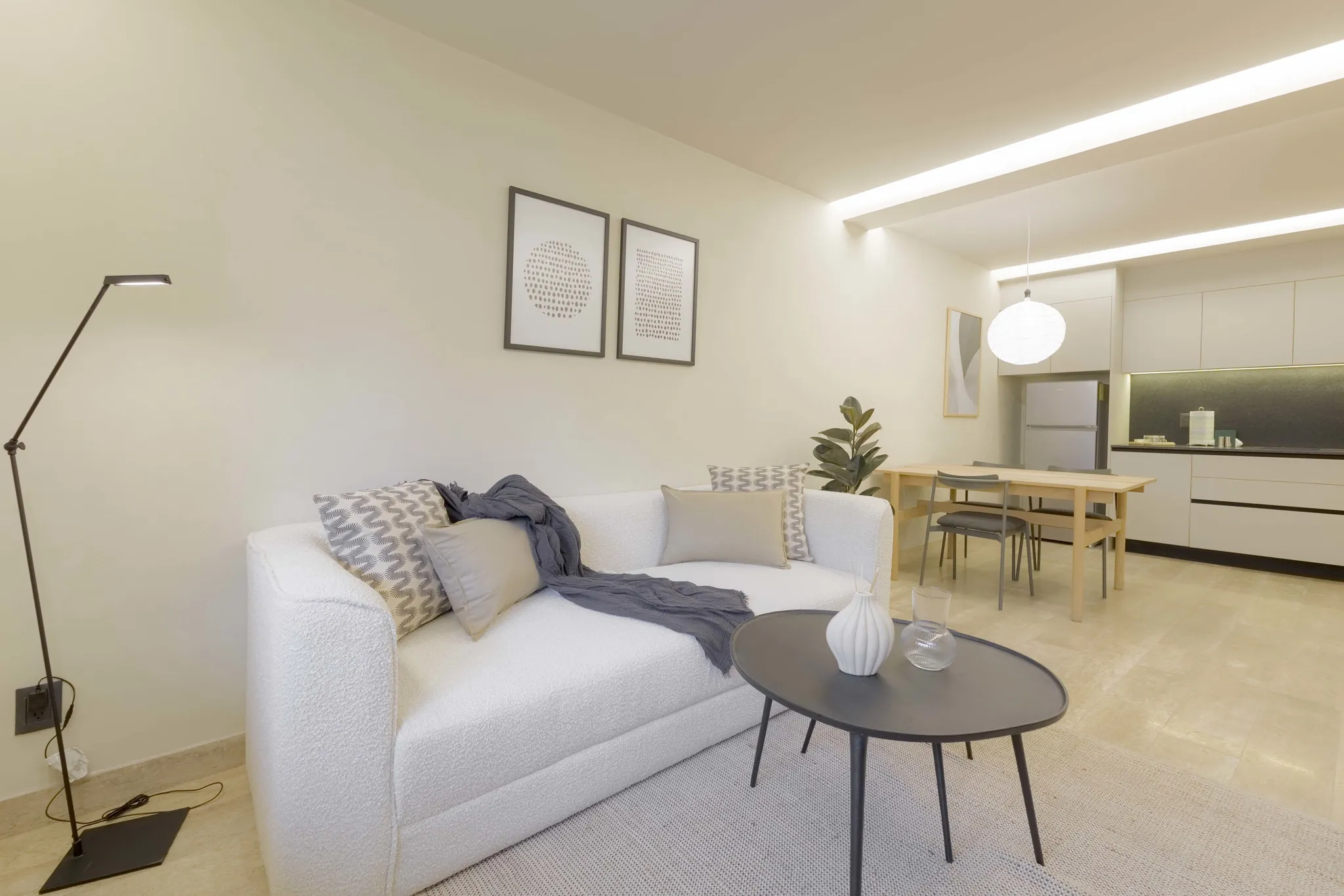 Modern living room with a white couch, coffee table, and dining area.