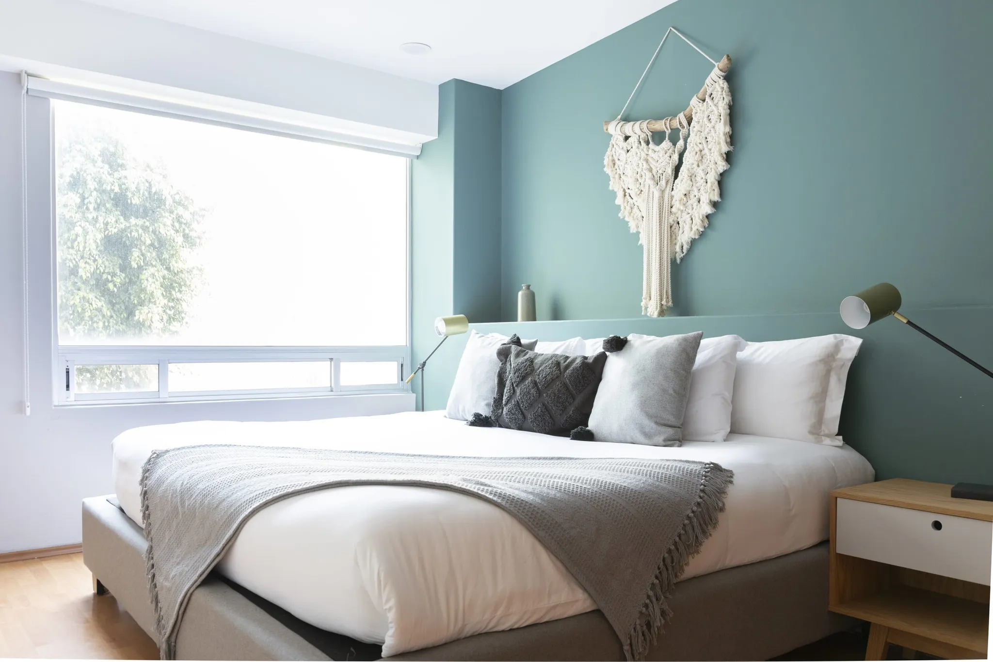 A bedroom with a large bed, minimalist decor, and a macrame wall hanging.