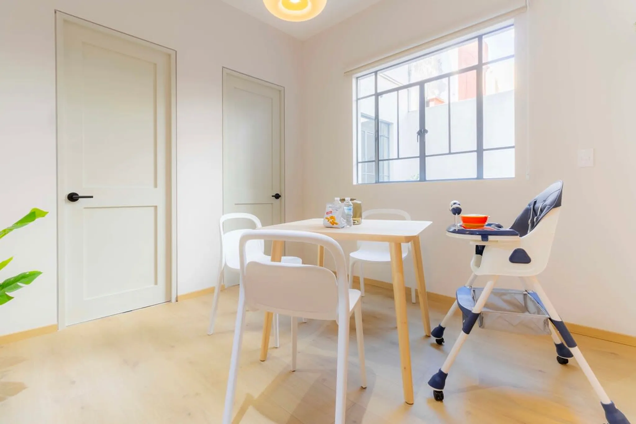 A dining set with a table, chairs, and a high chair is near a window.