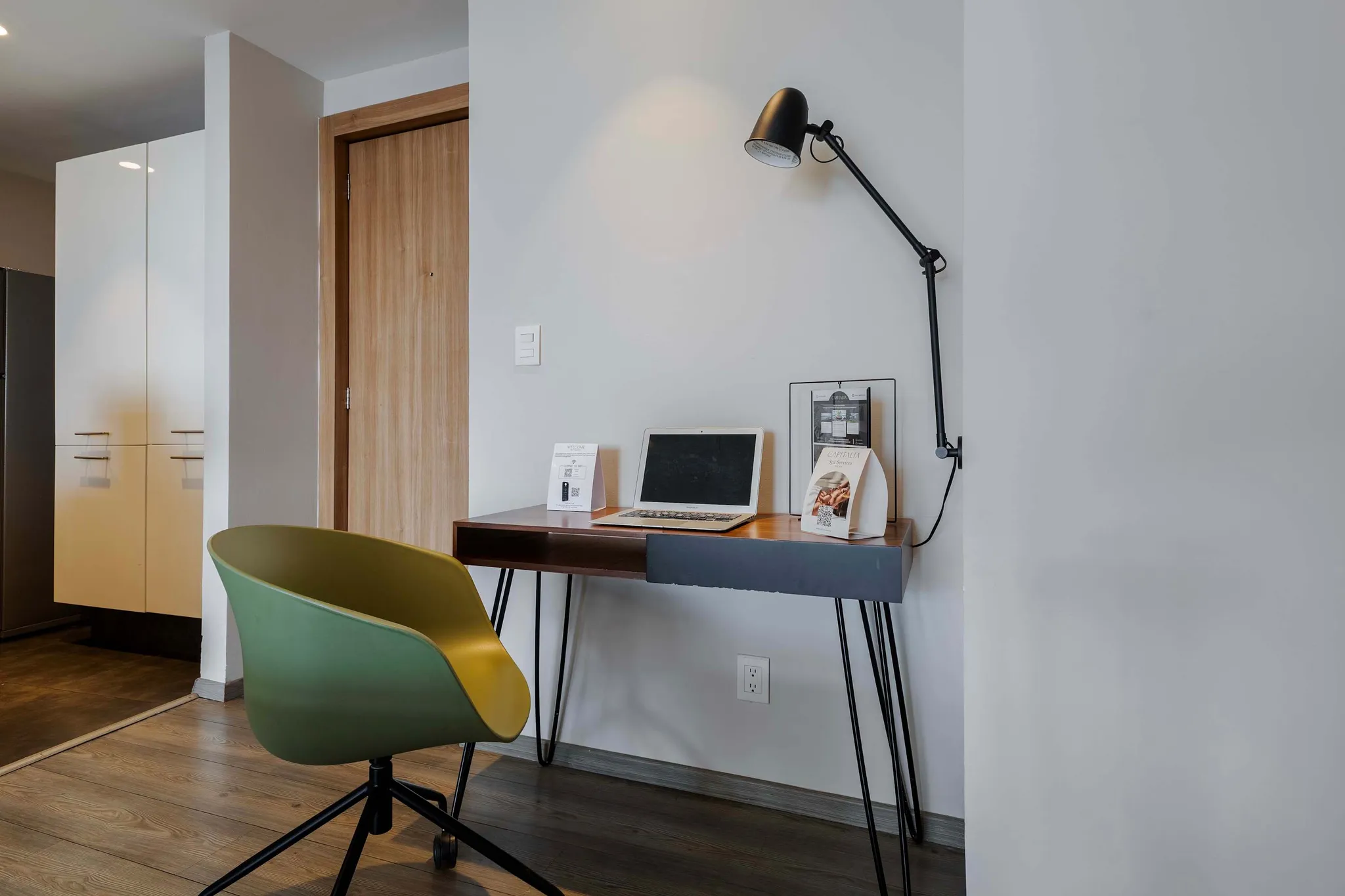 A home office nook with a laptop, desk lamp and green chair at Plaza Residences.