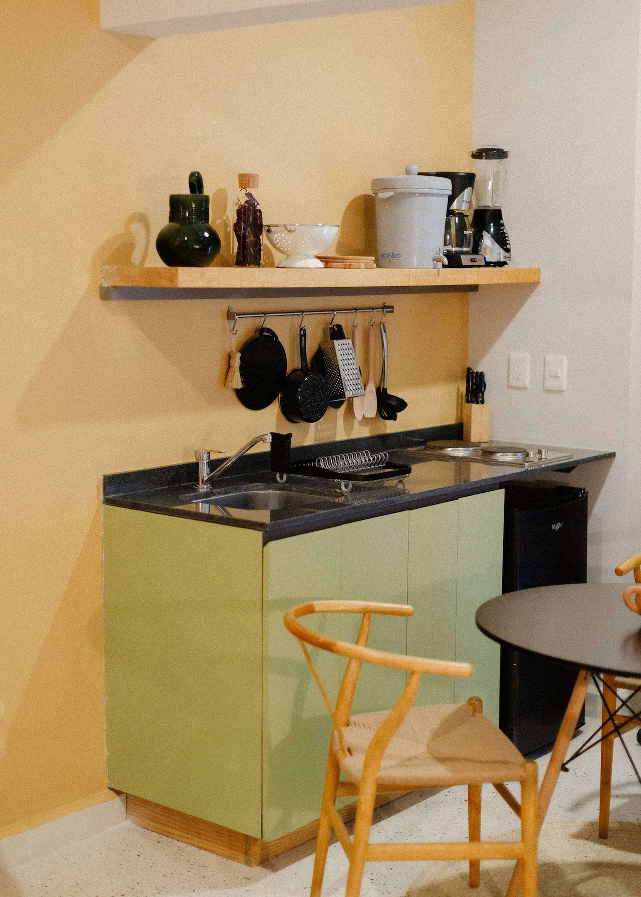 A light green kitchen with a sink, stove, and refrigerator, next to a wooden chair and table.