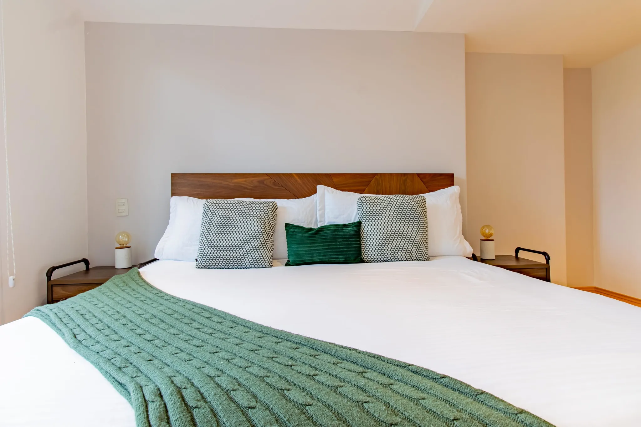 A large bed with white bedding, decorative pillows, and a green knit throw.