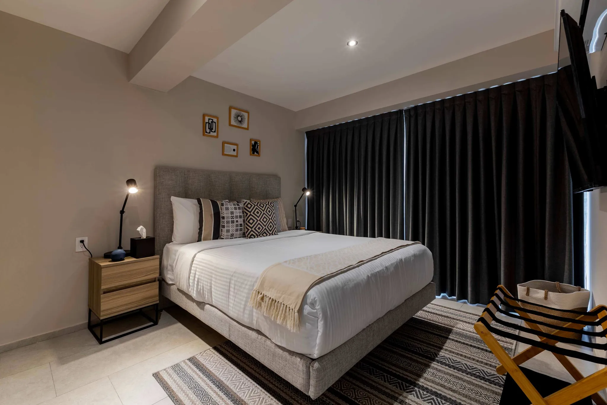 A modern bedroom with a king-size bed, bedside table, and dark curtains.