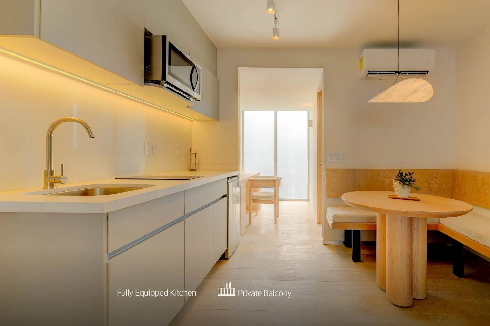 A modern kitchen with a sink, microwave, and dining area with a wooden table and benches.