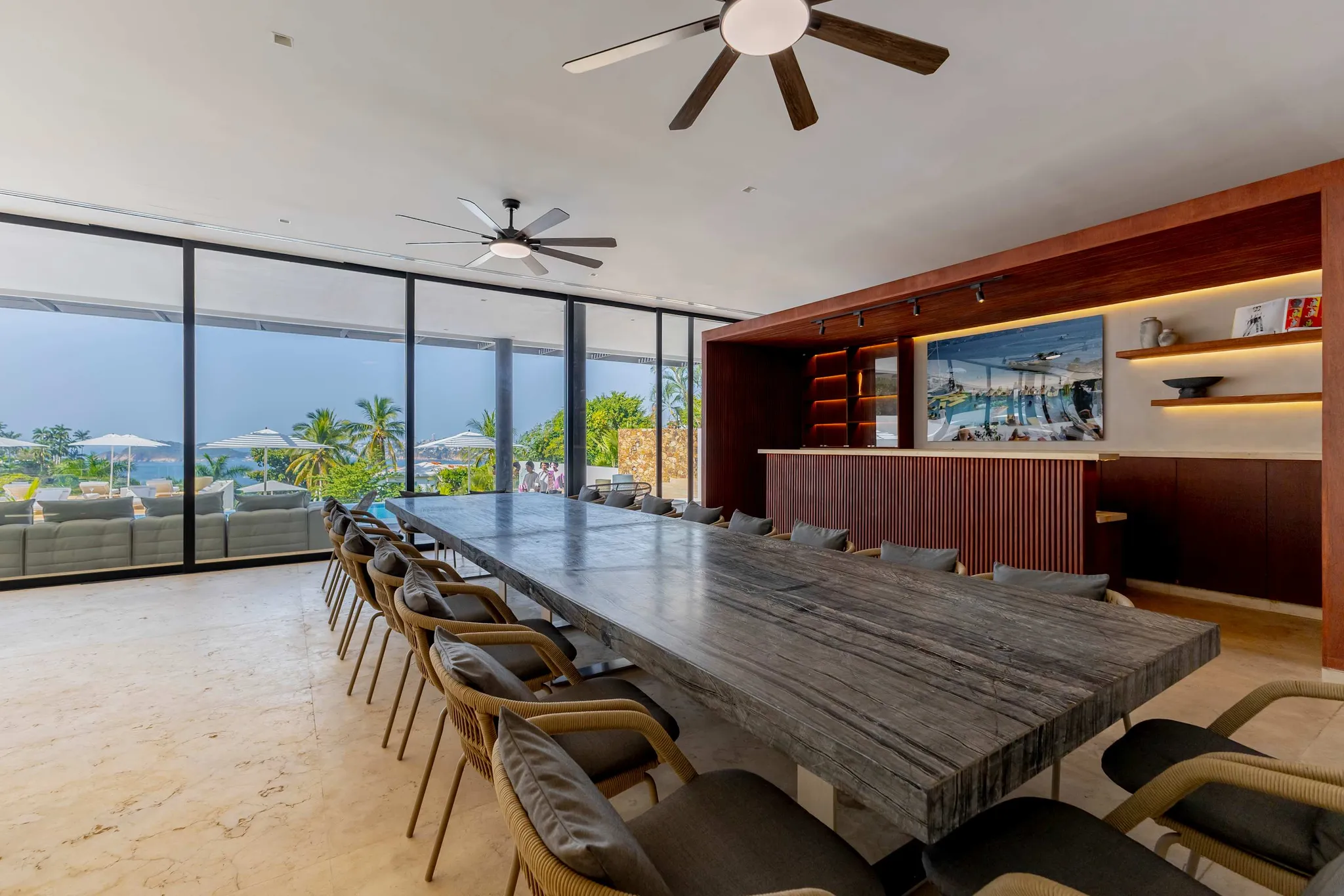 A spacious dining room with a large marble table, wicker chairs, and a view of the ocean.