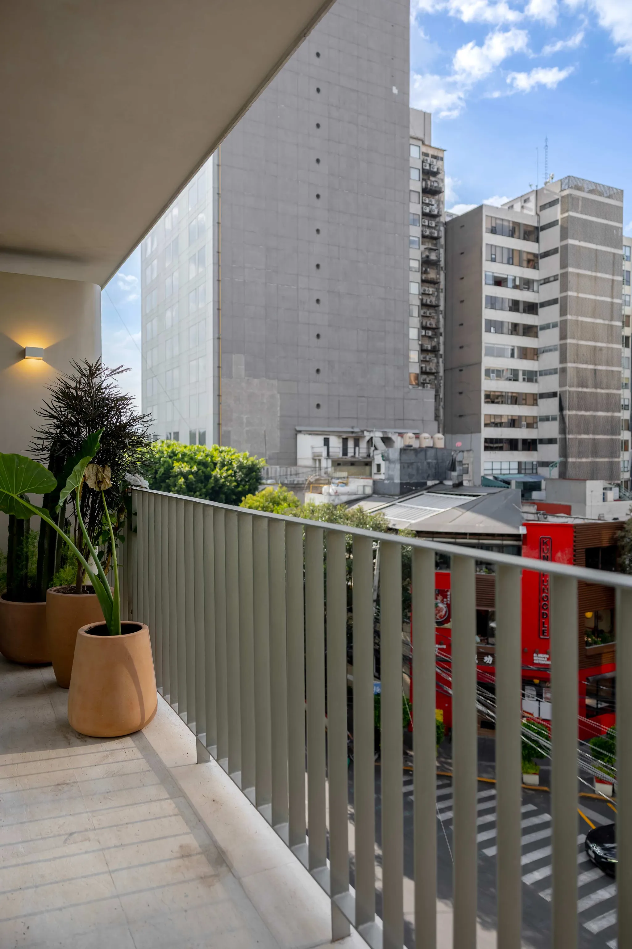 A balcony overlooking a city street with buildings and plants.