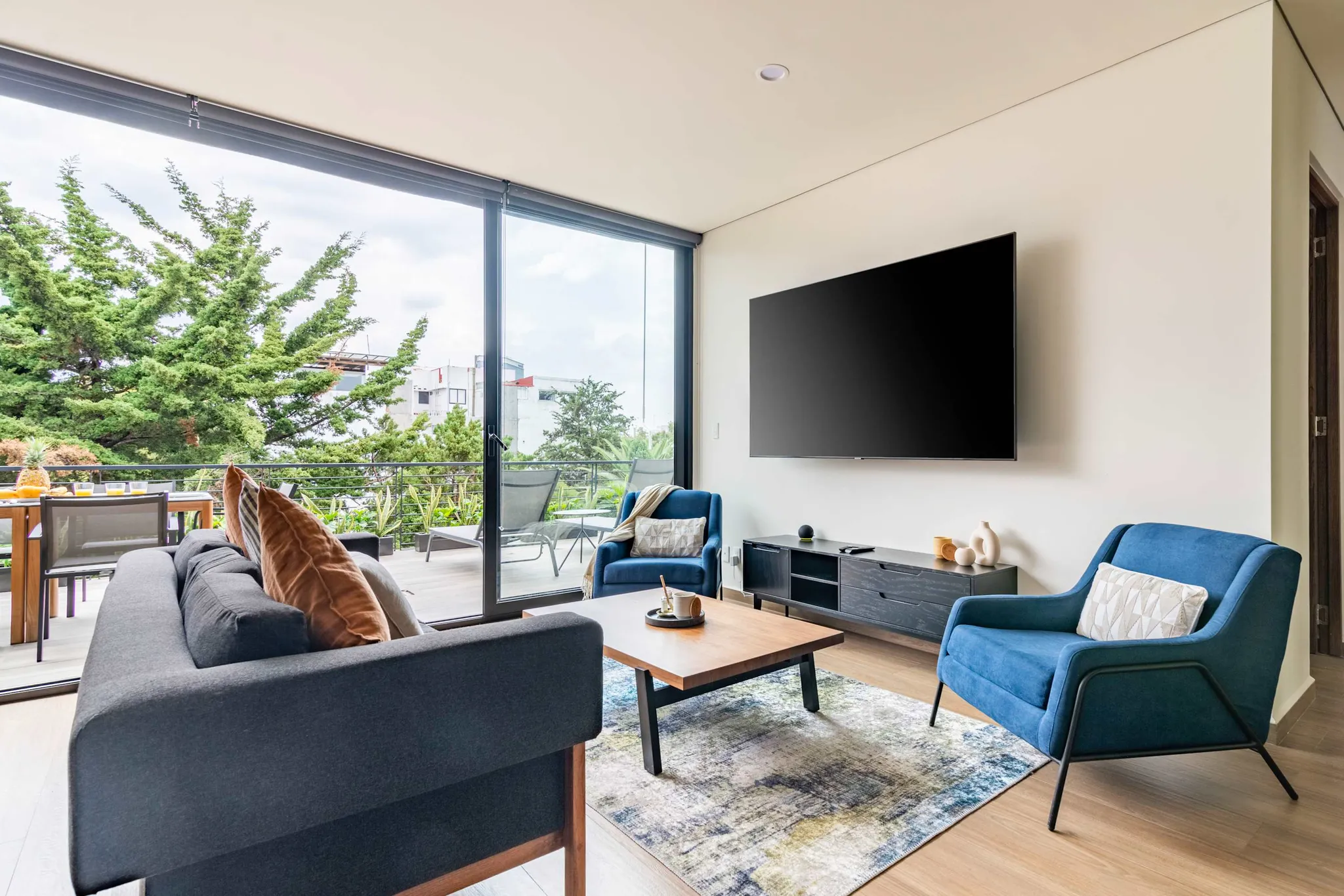A modern living room with a grey sofa, blue armchairs, and a large TV.