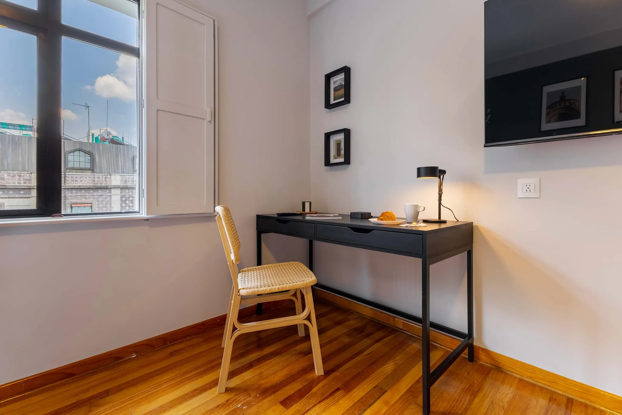 A desk and chair are set up in front of a window with a view of buildings.