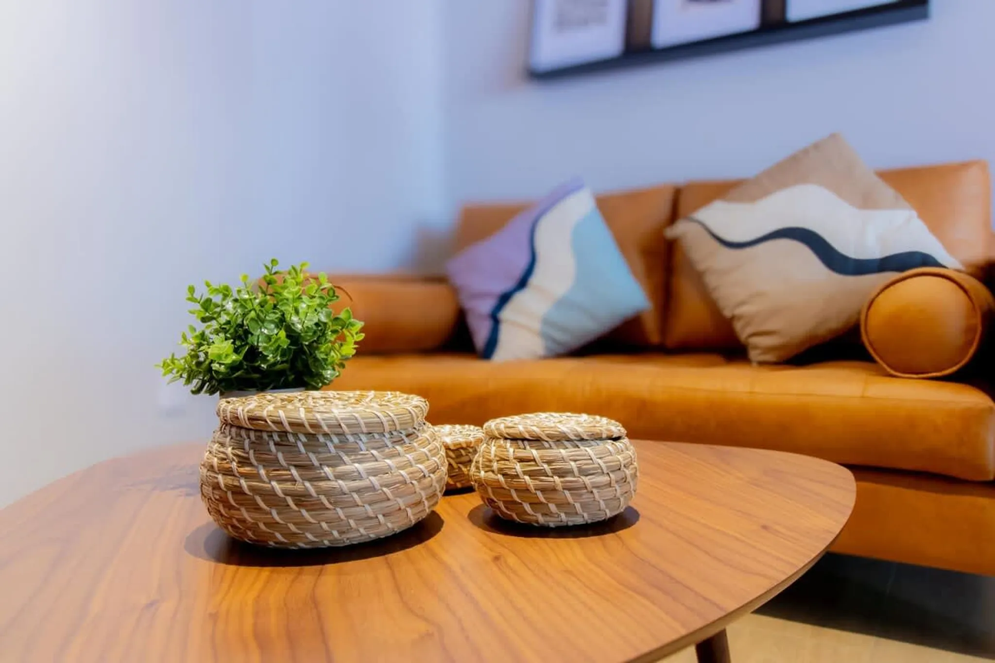 A coffee table with two woven baskets sits in front of a caramel-colored couch with decorative pillo