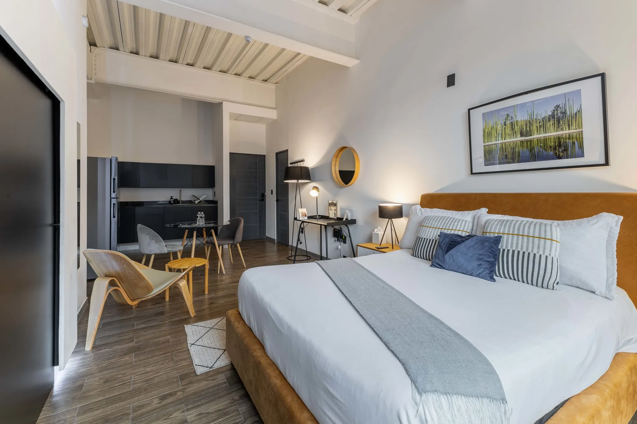 A king-sized bed with a tan headboard and blue and striped pillows in a modern room.