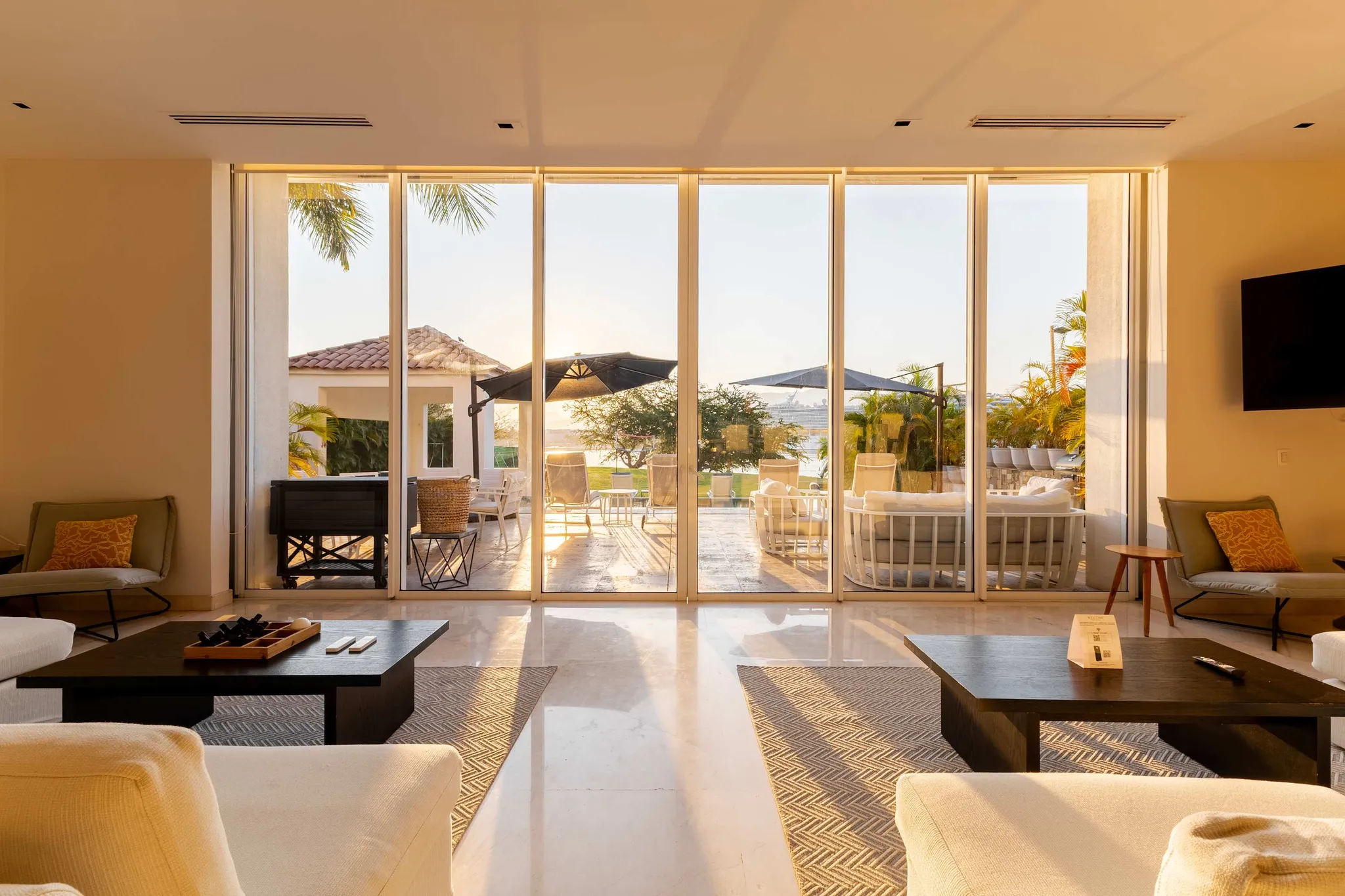 A modern living room with floor-to-ceiling windows offering a view of a patio and a body of water.