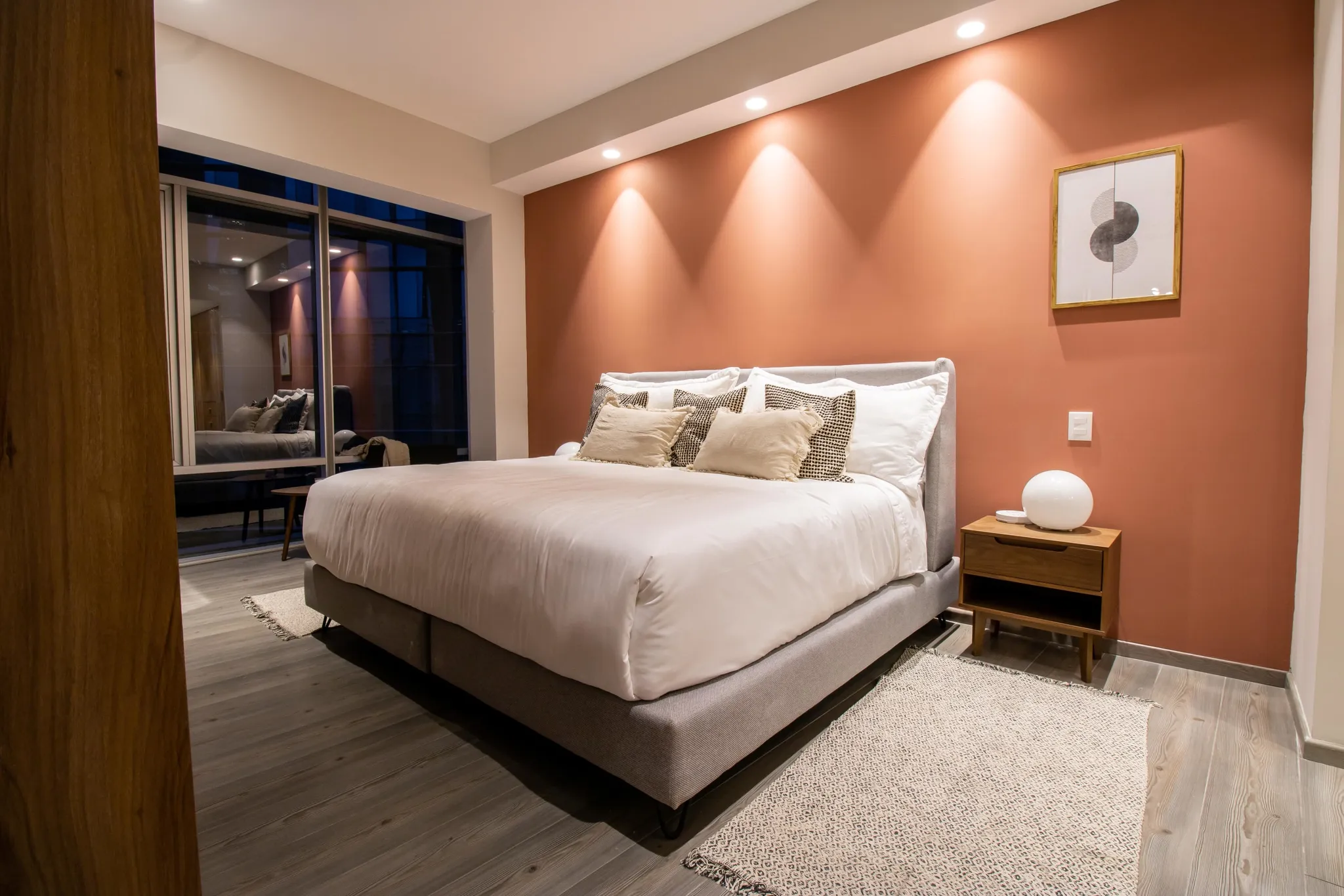 A modern bedroom with a king-size bed and a terracotta wall.