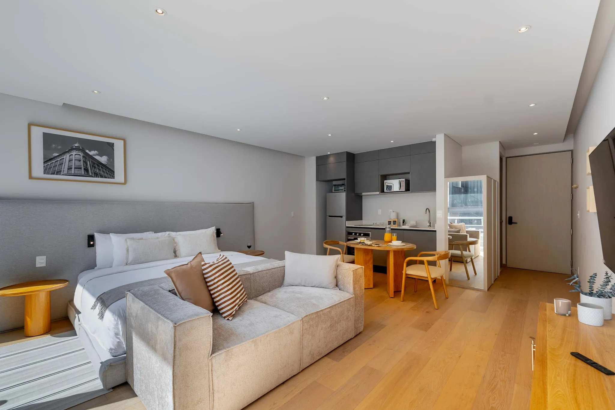 A modern studio apartment with a bed, sofa, kitchen, and dining area.