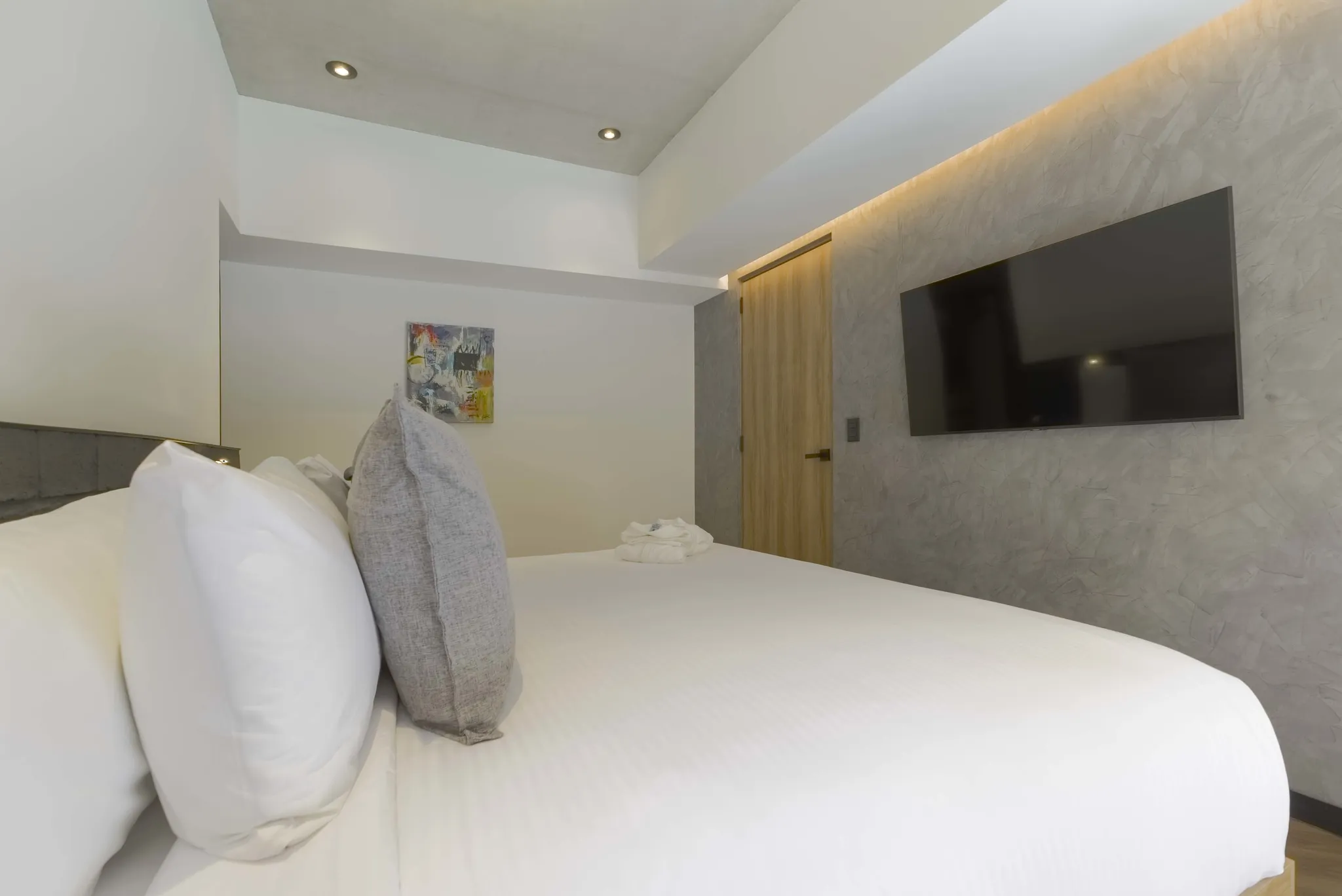 A bedroom with a bed, artwork, and a TV on a textured wall.